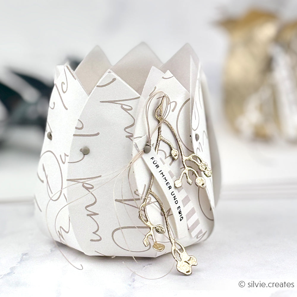 Weiße Papierlaterne von Alexandra Renke, gefertigt aus hochwertigem Designpapier, verziert mit goldenen Blumenakzenten und eleganter Schrift, versehen mit einem kleinen deutschen Anhänger.