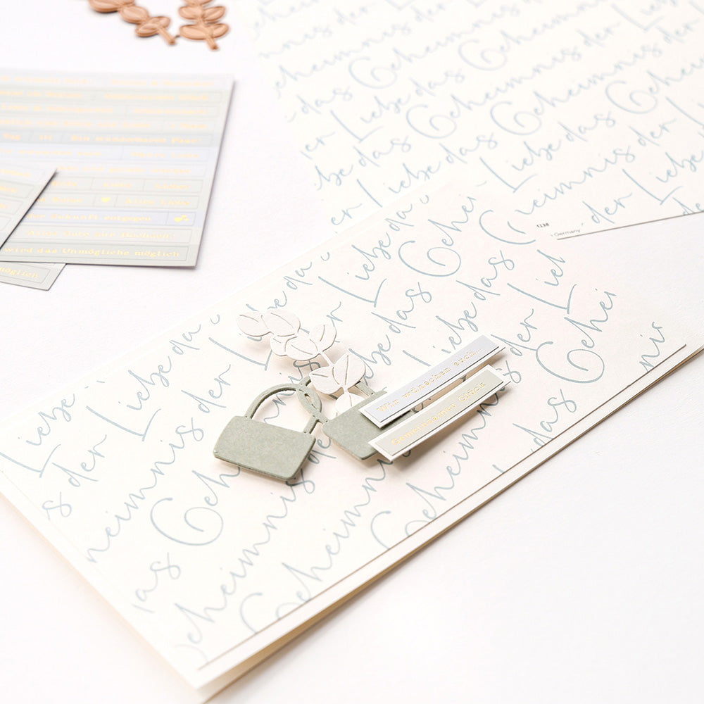 Flaches Layout aus handgeschriebenen Papieren, Alexandra Renke Designpapier, Büroklammern, Aufklebern und dekorativen Ausschnitten auf Weiß - die perfekte Inspiration für Fans von Papierprojekten oder Buchbinderei.