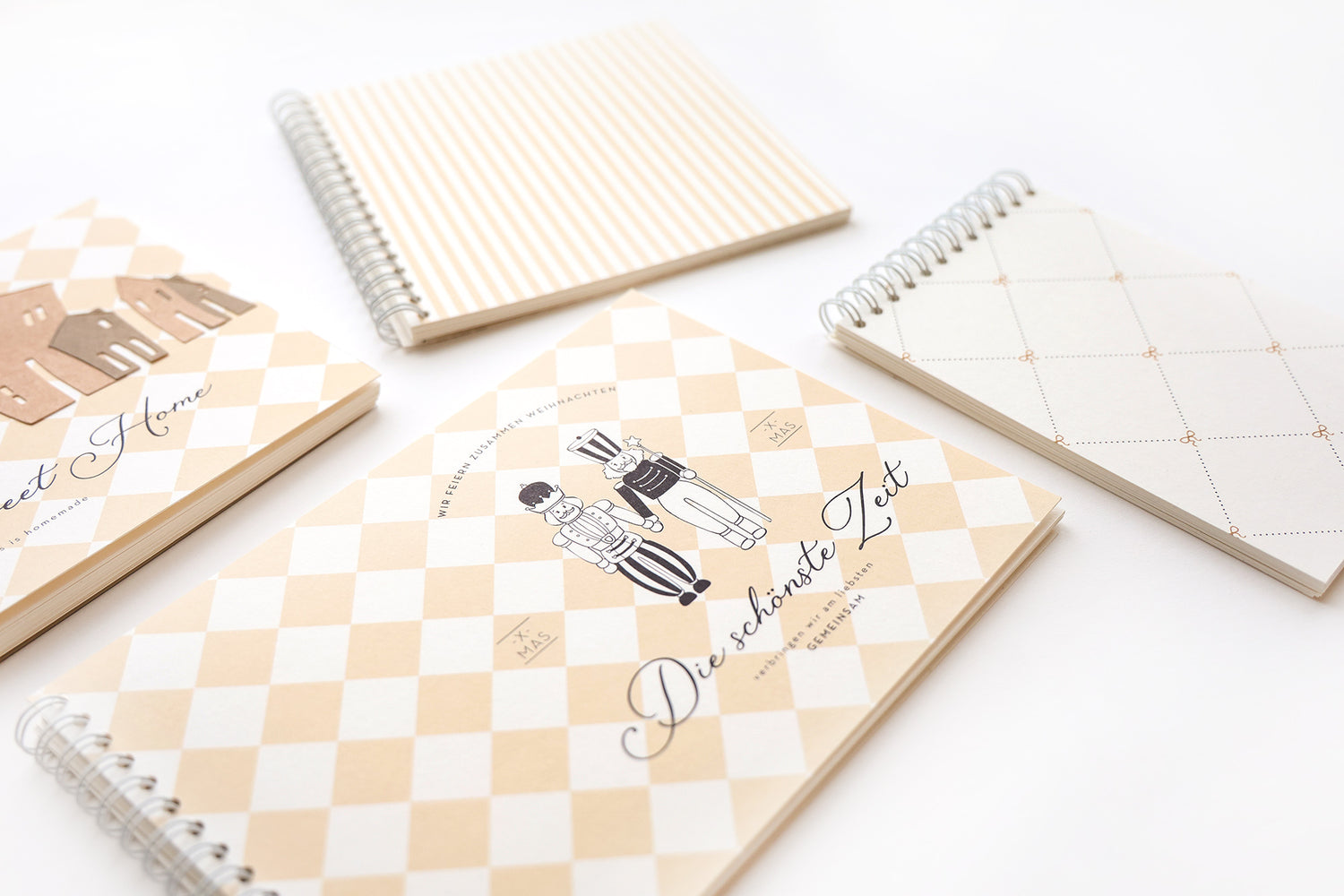 Vier spiralgebundene Notizbücher mit beigefarbenem, kariertem und gestreiftem Einband, eines mit der Aufschrift Die schönste Zeit.