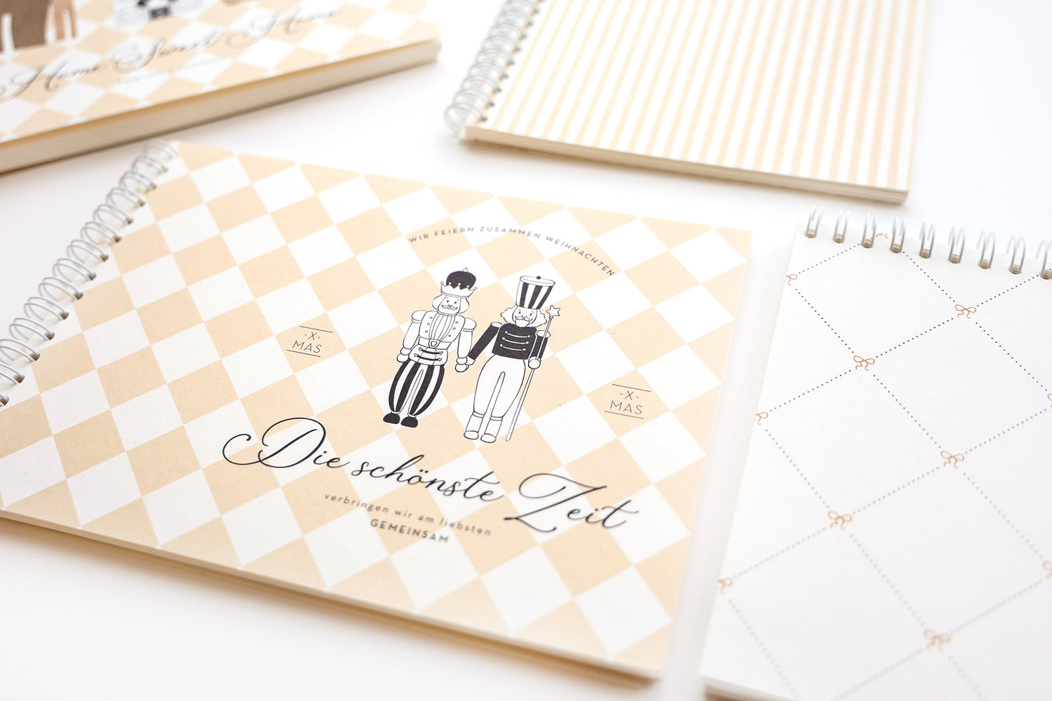 Spiralgebundene beige-weiße Notizbücher mit Rautenmuster und deutschem Text auf weißer Oberfläche.
