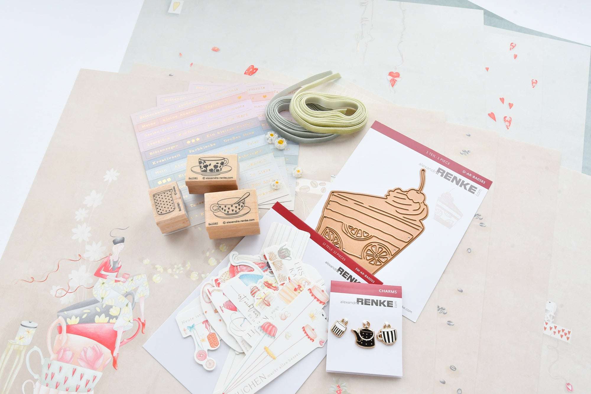 Verschiedene Schreibwaren, Stempel, Bänder und dekorative Papiere mit Tee- und Dessertmotiven auf einer weißen Fläche.