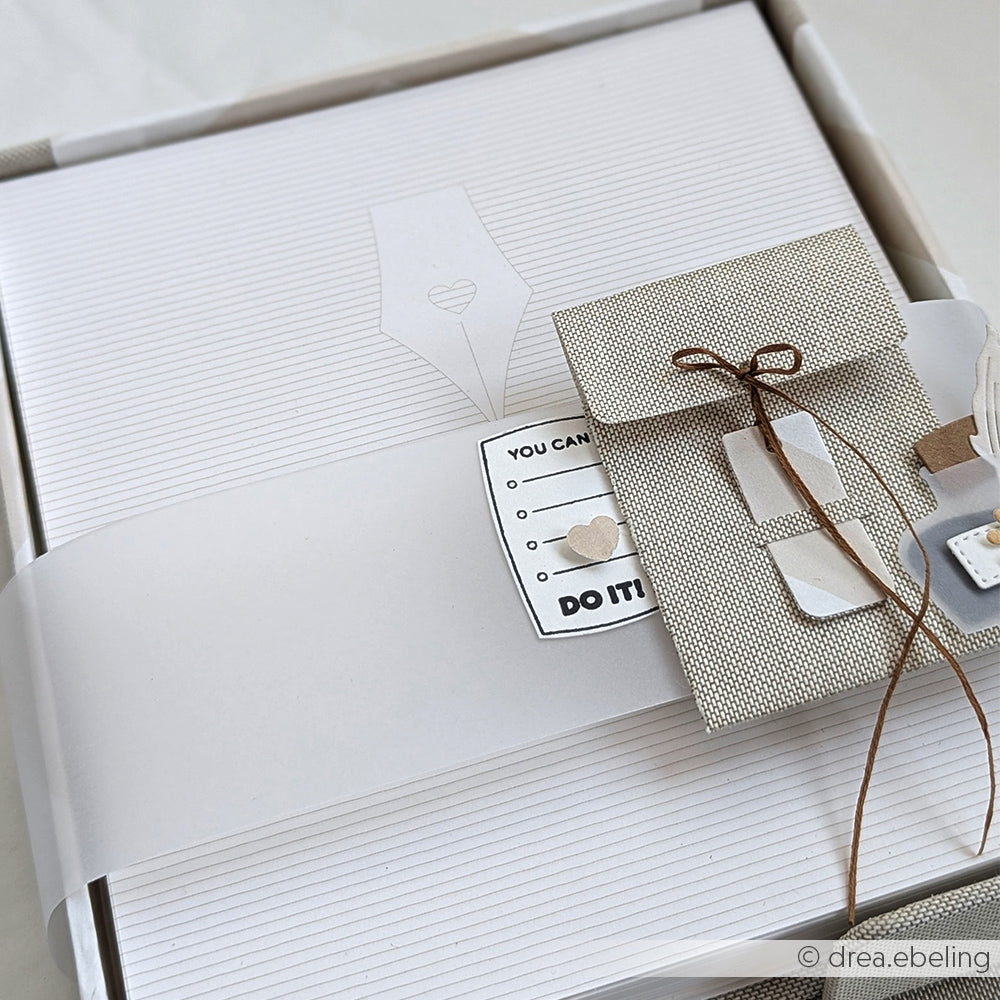 Eine hübsch verpackte Geschenkschachtel mit einem kleinen Umschlag und einer Karte, verschnürt mit brauner Schnur, auf weißem Hintergrund - hergestellt aus hochwertigen Alexandra Renke Graupappe Zuschnitten für eine robuste Verarbeitung.