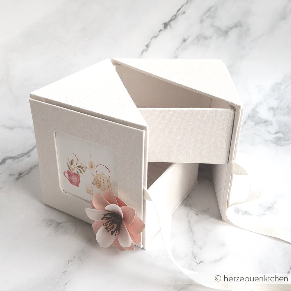 Cremefarbene Geschenkbox von Alexandra Renke mit Schleife, Blumendekoration und Teekannen-Illustration auf Marmor - ideal als elegantes PAPPKit oder Fotowürfelbox für besondere Anlässe.