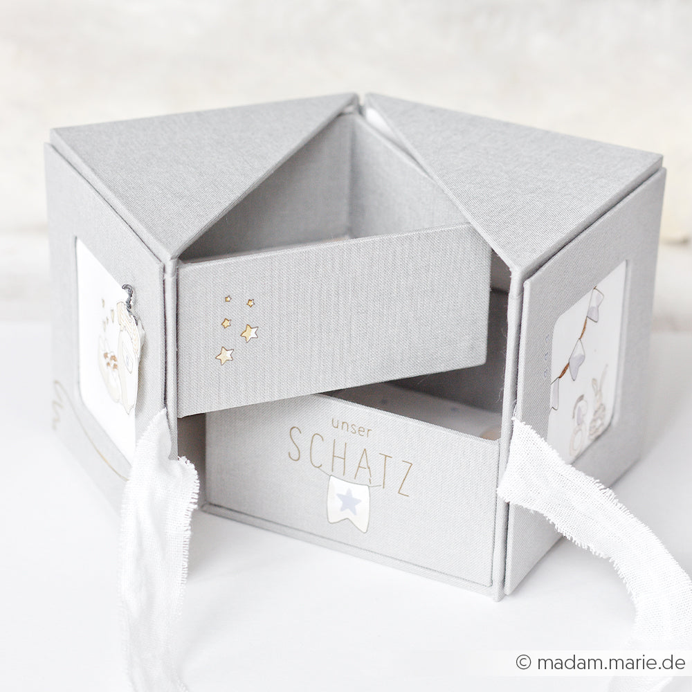 Graue sechseckige Erinnerungsbox mit weißem Band, aufklappbar mit Fächern und der Aufschrift unser SCHATZ - eine einzigartige Fotowürfelbox von Alexandra Renke, perfekt zum Aufbewahren Ihrer besonderen Erinnerungen.