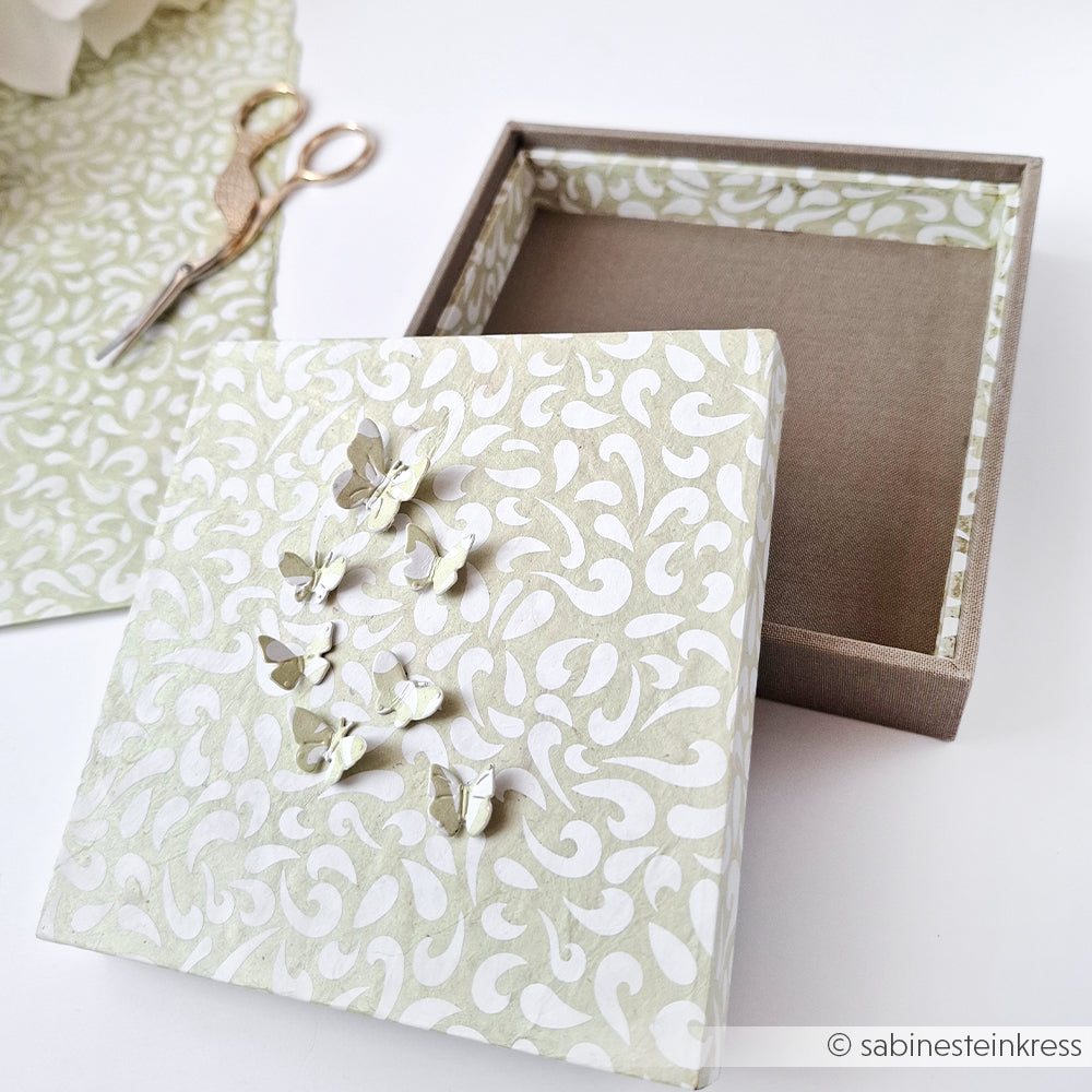Gestalten Sie eine einzigartige Geschenkverpackung mit der Alexandra Renke Einsteckbox mit weißen Mustern und Schmetterlingen aus Papier - öffnen Sie neben Schere und Stoff, um sich von Ihrem PAPPKit zum Basteln Ihrer Geschenkverpackung inspirieren zu lassen.