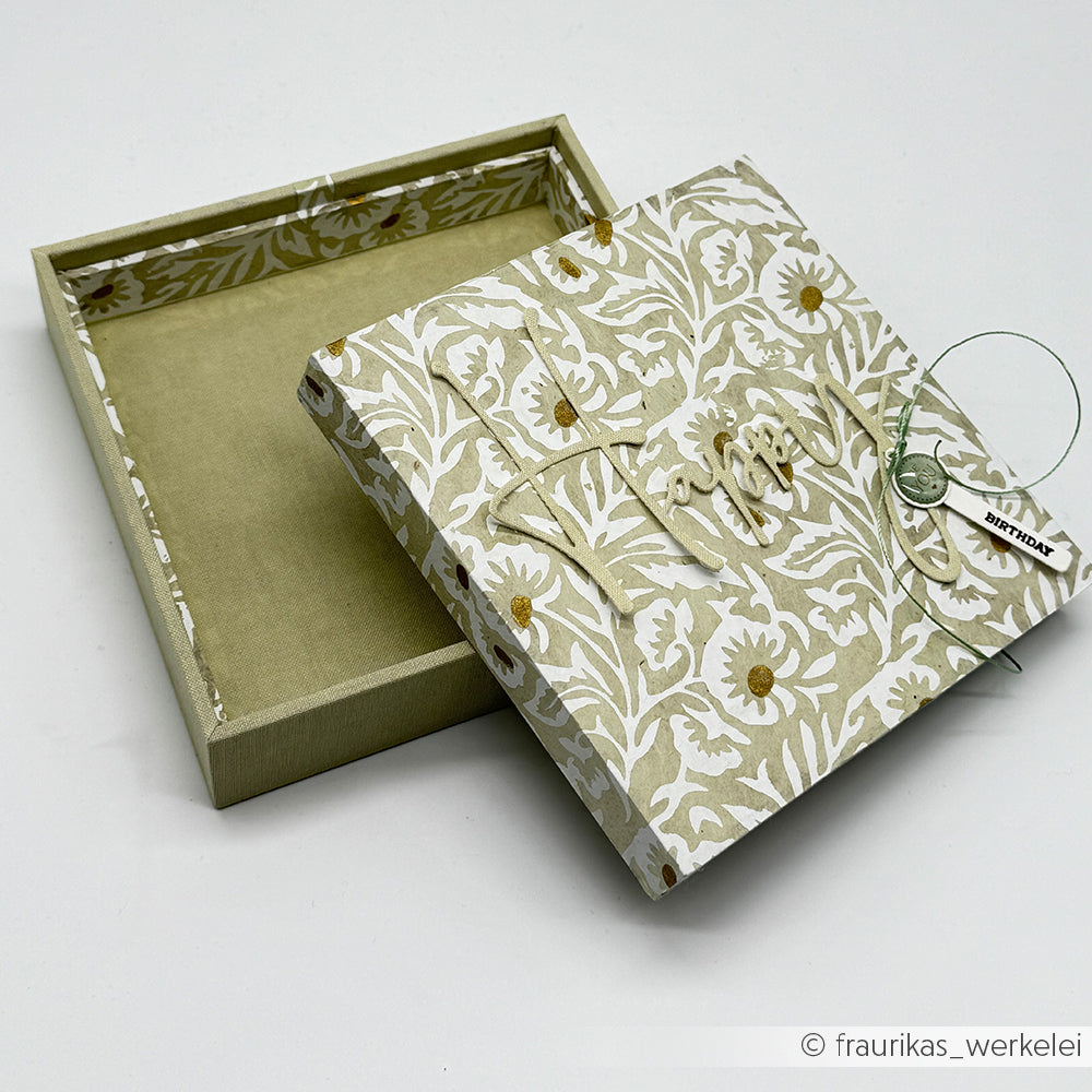 Eine floral gemusterte Alexandra Renke Einsteckbox mit "Happy Birthday" auf dem Deckel, teilweise aus dem Boden genommen - ideal für stilvolle Geschenkverpackungen.