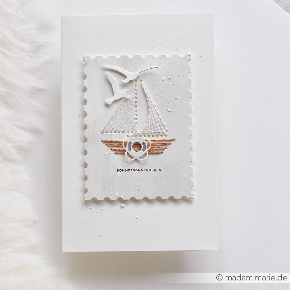 Weiße Karte von Alexandra Renke mit einem Segelboot aus Papier, einem Vogel und dem deutschen Schriftzug „SOMMERSONNENGRUSS“ auf einem strukturierten Rechteck, gefertigt mit hochwertigen Stanzsystemen und Designpapieren für einen eleganten Touch.