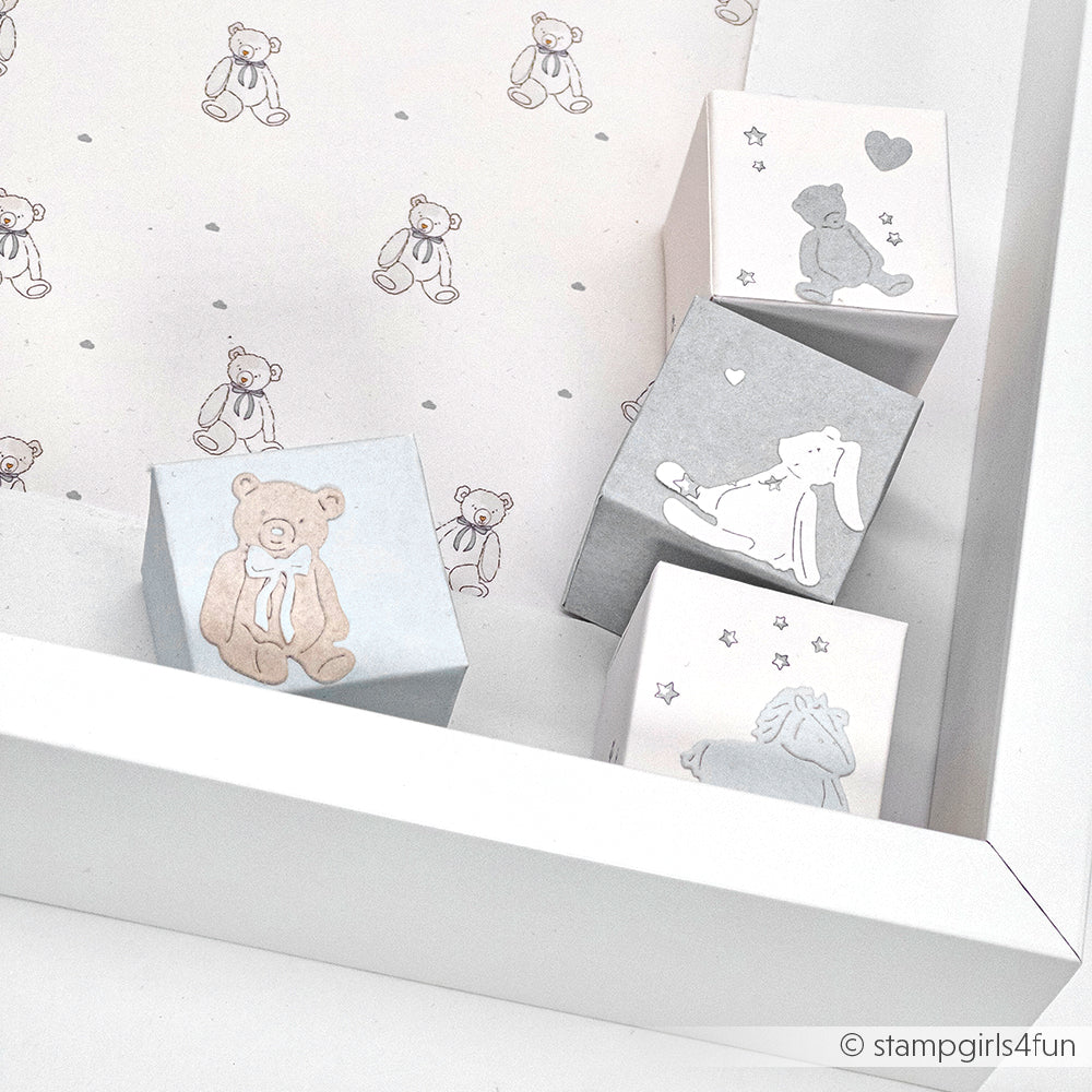 Pastellfarbene Blöcke mit Tierillustrationen ruhen auf einer weißen Fläche vor einem Hintergrund aus teddybärgemusterten Designpapieren von Alexandra Renke.