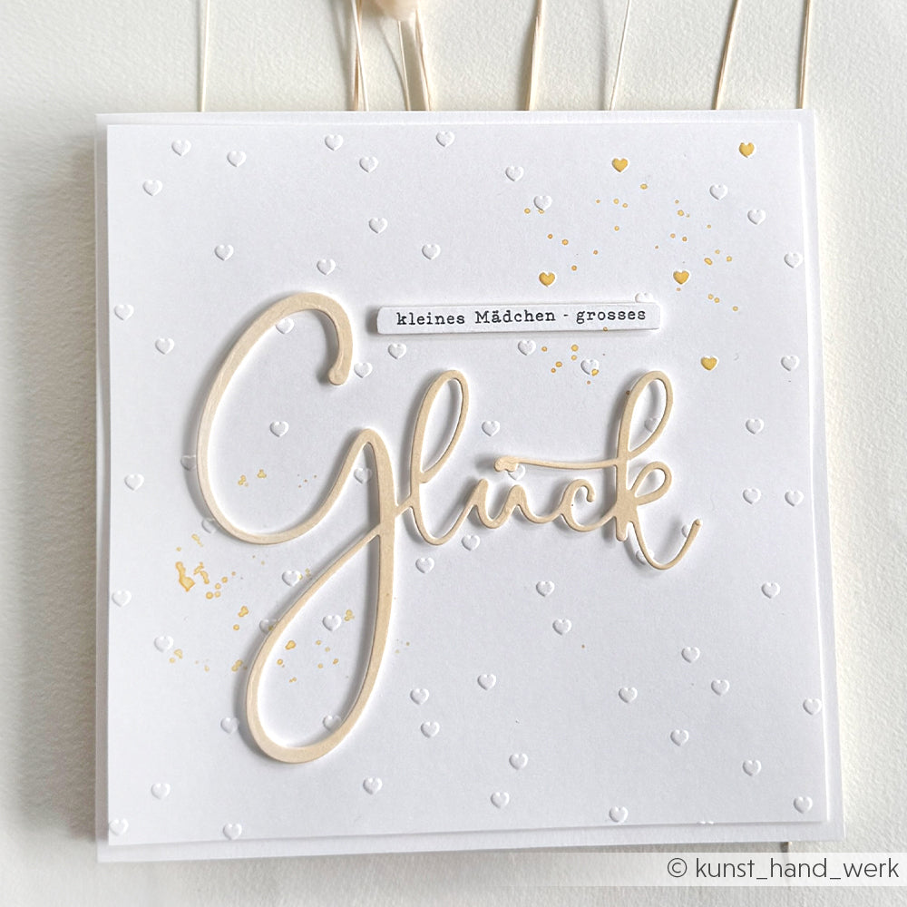 Weiße Grußkarte von Alexandra Renke, die mit einem Prägefolder hergestellt wurde. Mit geprägten Herzen, goldenen Akzenten und dem Spruch "Kleines Mädchen, grosses Glück".