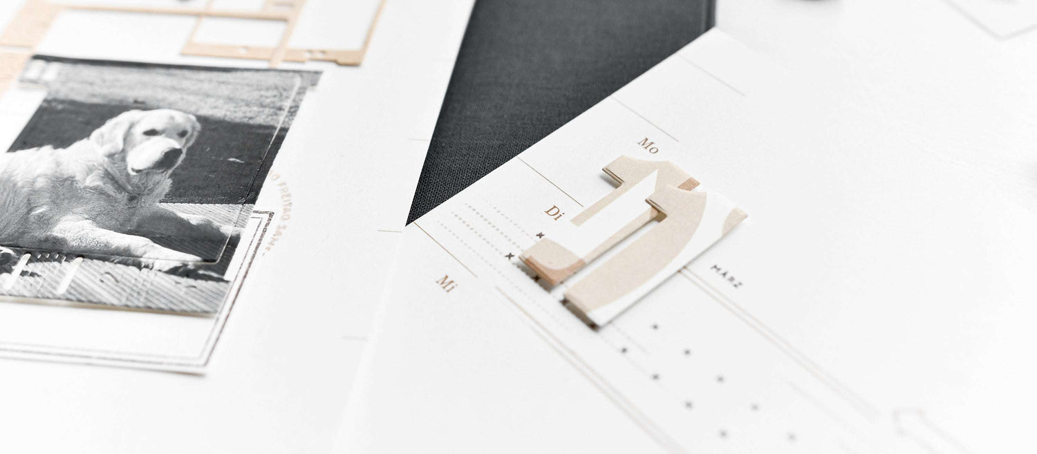 Nahaufnahme eines Fotos von einem Hund und einem Papierausschnitt Nummer eins auf einem weißen, minimalistischen Kalender- oder Planerblatt.