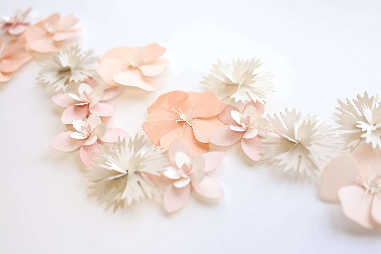Papierblumen in zarten Rosa- und Beigetönen, arrangiert auf einer weißen Fläche.