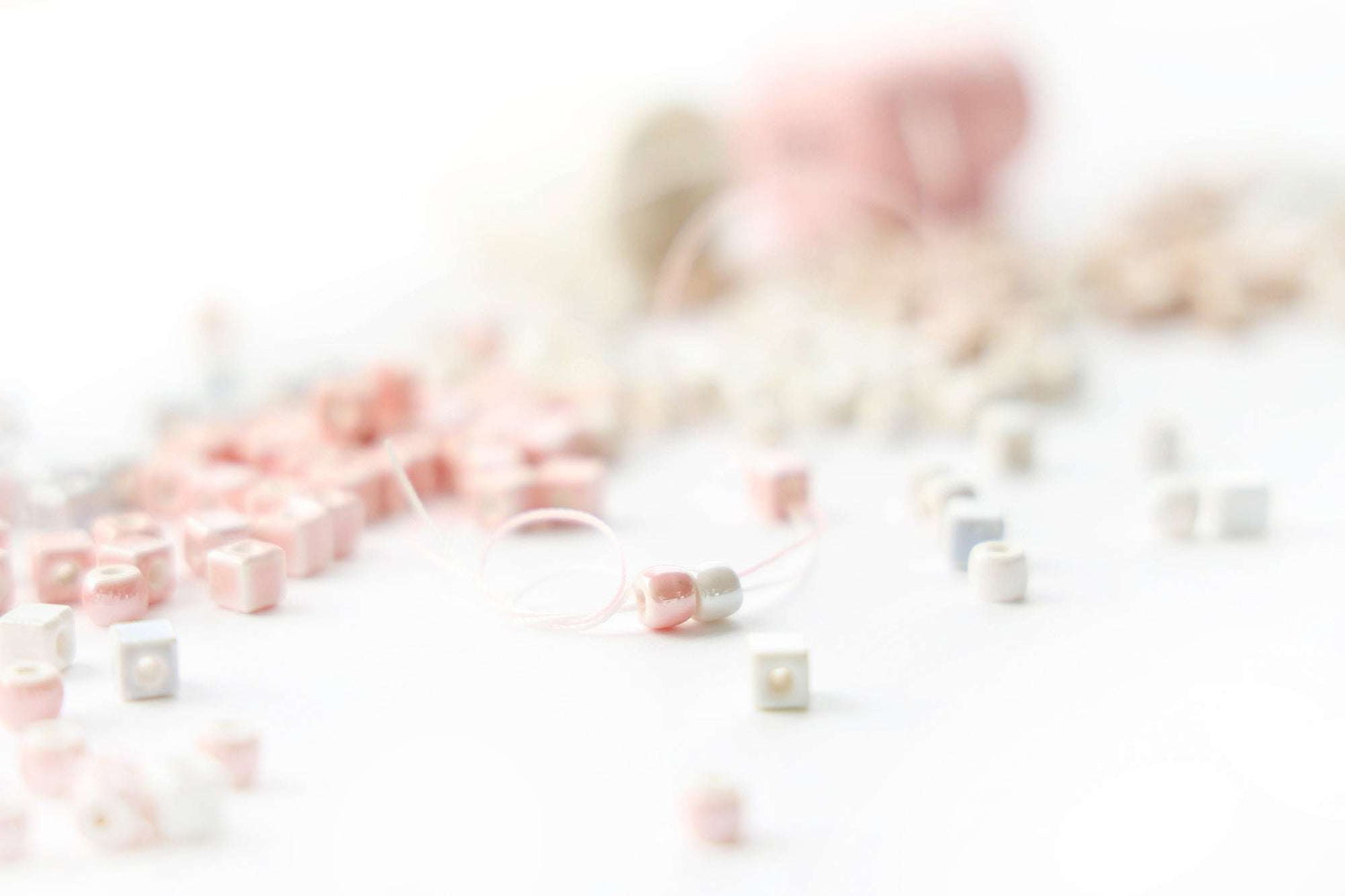 Nahaufnahme von pastellrosa und weißen Perlen auf einer Schnur, mit weiteren Perlen im Hintergrund.