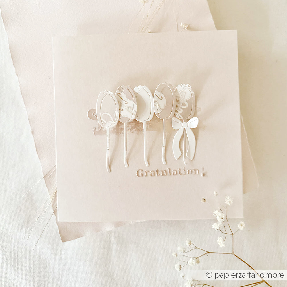 Quadratische, cremefarbene Karte von Alexandra Renke mit weißen 3D-Tulpen und dem Text "Gratulation!", hergestellt mit wiederverwendbaren Schablonen auf einem hellen, strukturierten Hintergrund, der mit kleinen Blumen verziert ist.