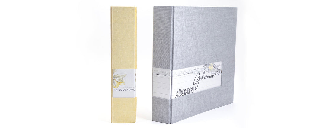 Gelber Schuber und grauer Ordner mit "KÜCHEN Geheimnis"-Etikett.