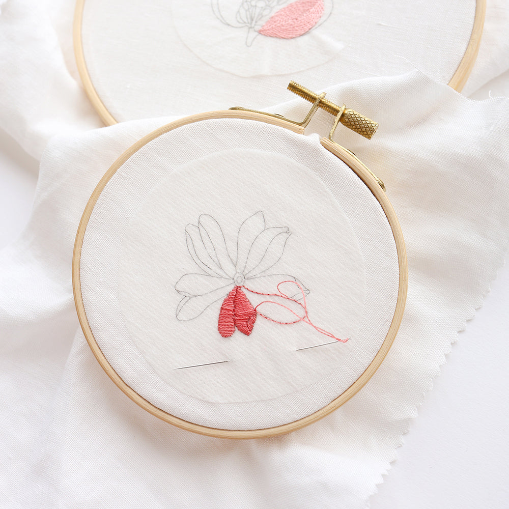 Stickrahmen von Alexandra Renke mit einem floralen Umriss; zwei Blütenblätter sind in Rot auf weißem Stoff gestickt – ideal für kreative Projekte oder als Stickvorlagen, wenn Sie Kleidung mit einer persönlichen Note gestalten möchten.