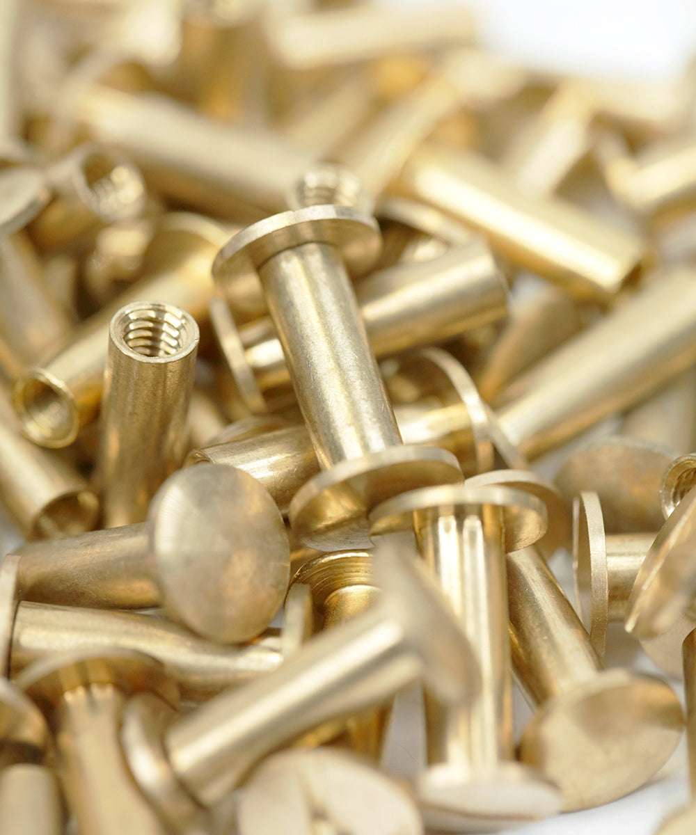 Ein Stapel Messingzylindermuttern mit flachen Köpfen und Innengewinde, in Nahaufnahme gezeigt.