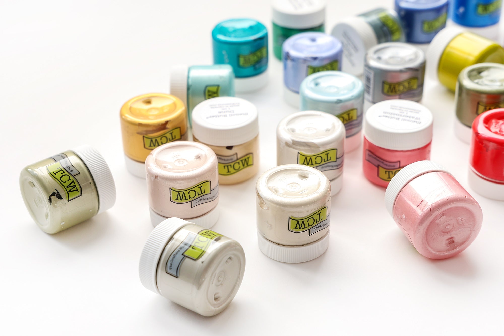 Kleine Tiegel mit bunter Farbe, die auf einer weißen Fläche angeordnet sind, einige stehen, andere liegen auf der Seite.