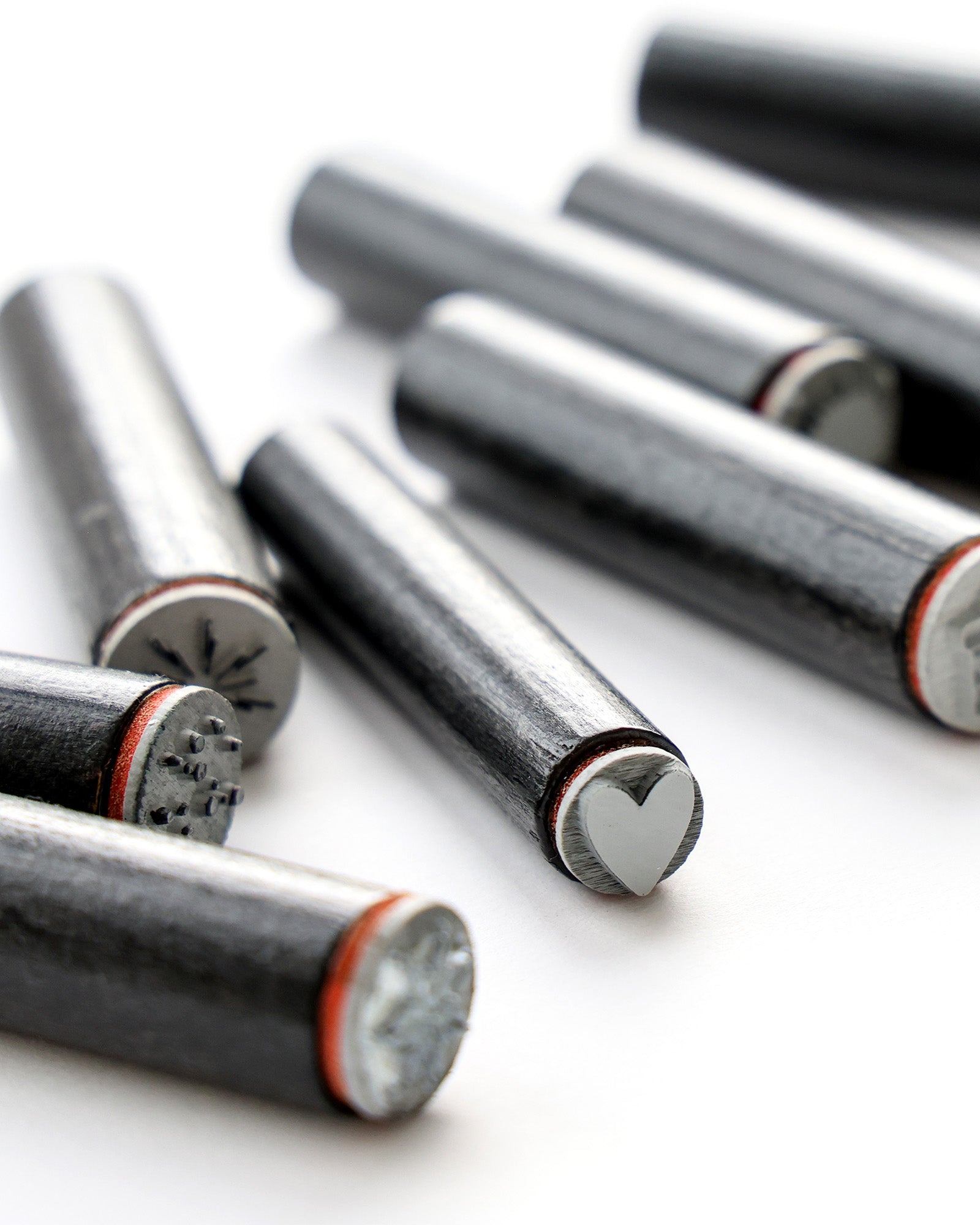 Metallstempel mit verschiedenen Formen an den Enden, darunter ein Herz, die auf einer weißen Fläche angeordnet sind.