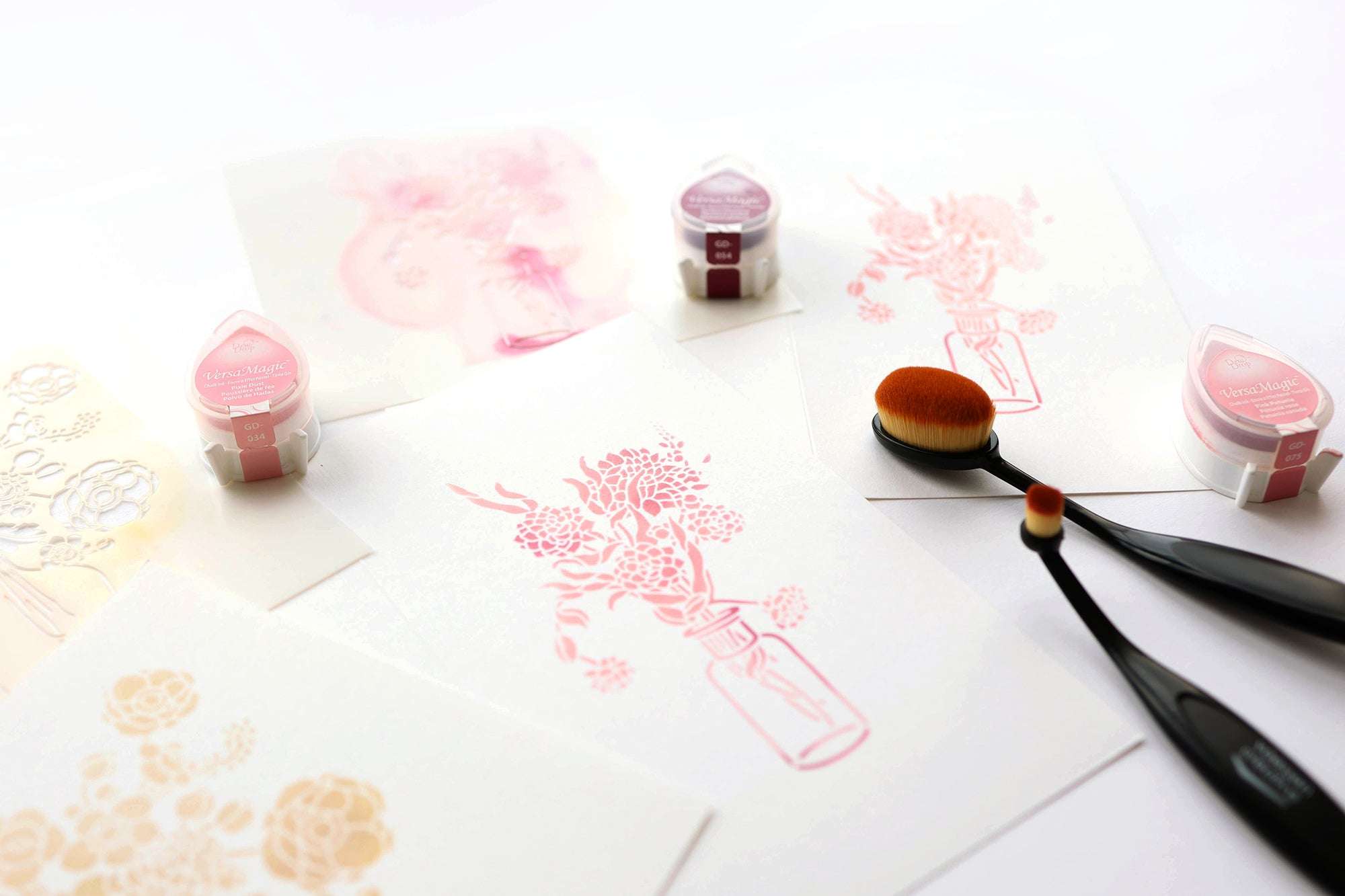 Rosa Blumendrucke auf weißem Papier, Stempelkissen und Mischpinsel auf einer weißen Fläche.