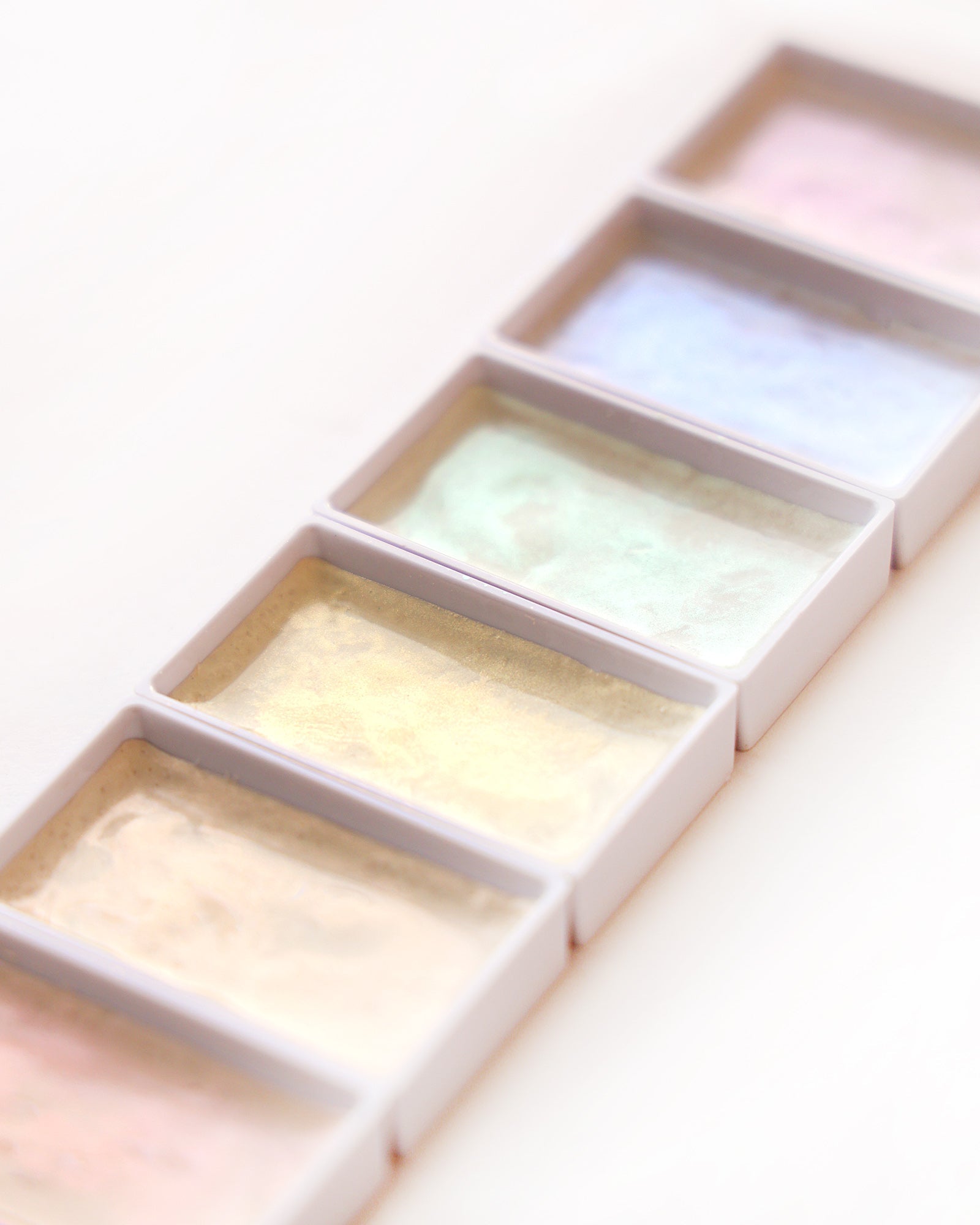 Kleine Aquarellfarbtöpfe und Farbfelder in verschiedenen Farben, die auf einer weißen Fläche angeordnet sind.