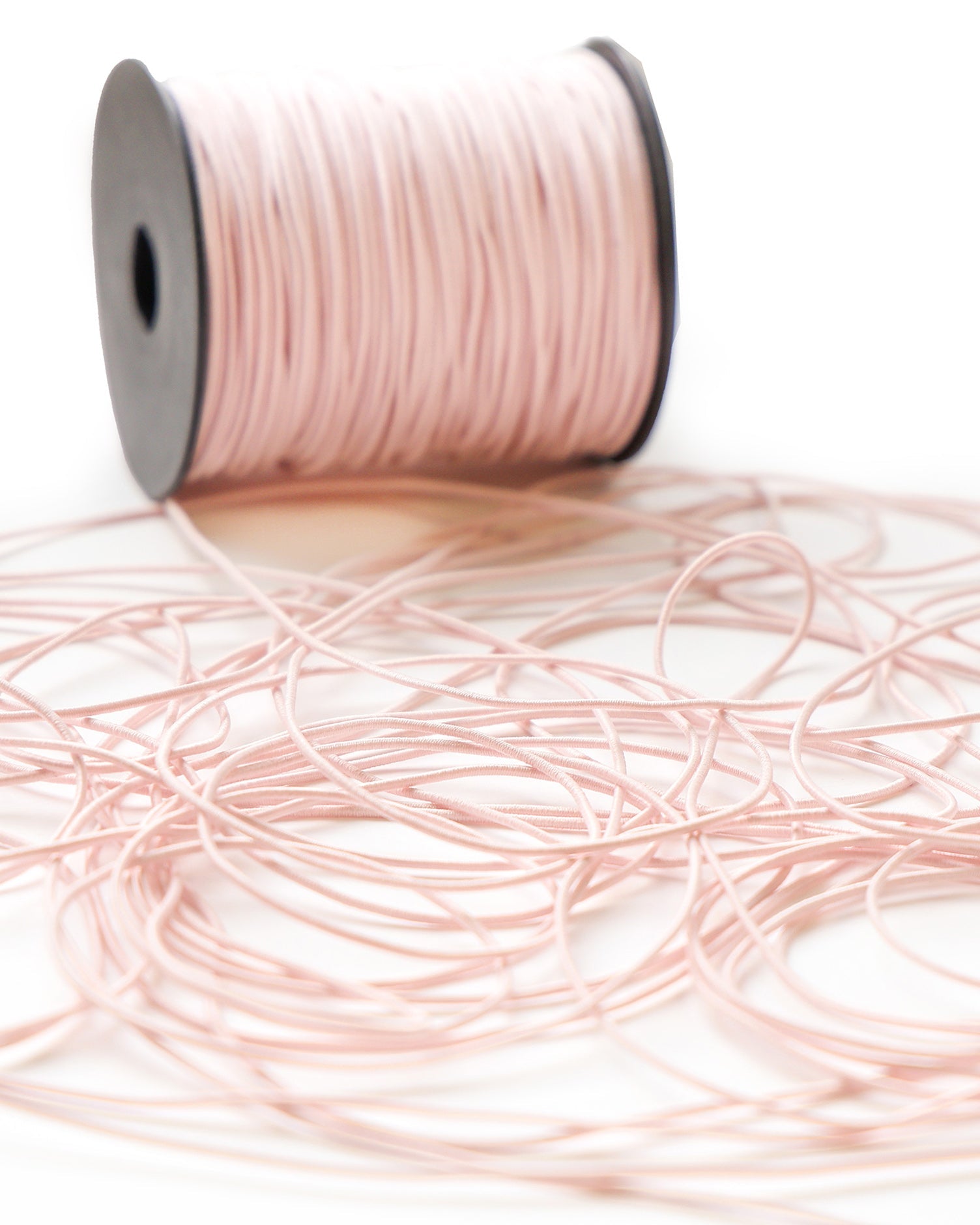 Eine Spule mit blassrosa elastischer Kordel, deren lose Längen auf einer weißen Fläche ausgebreitet sind.