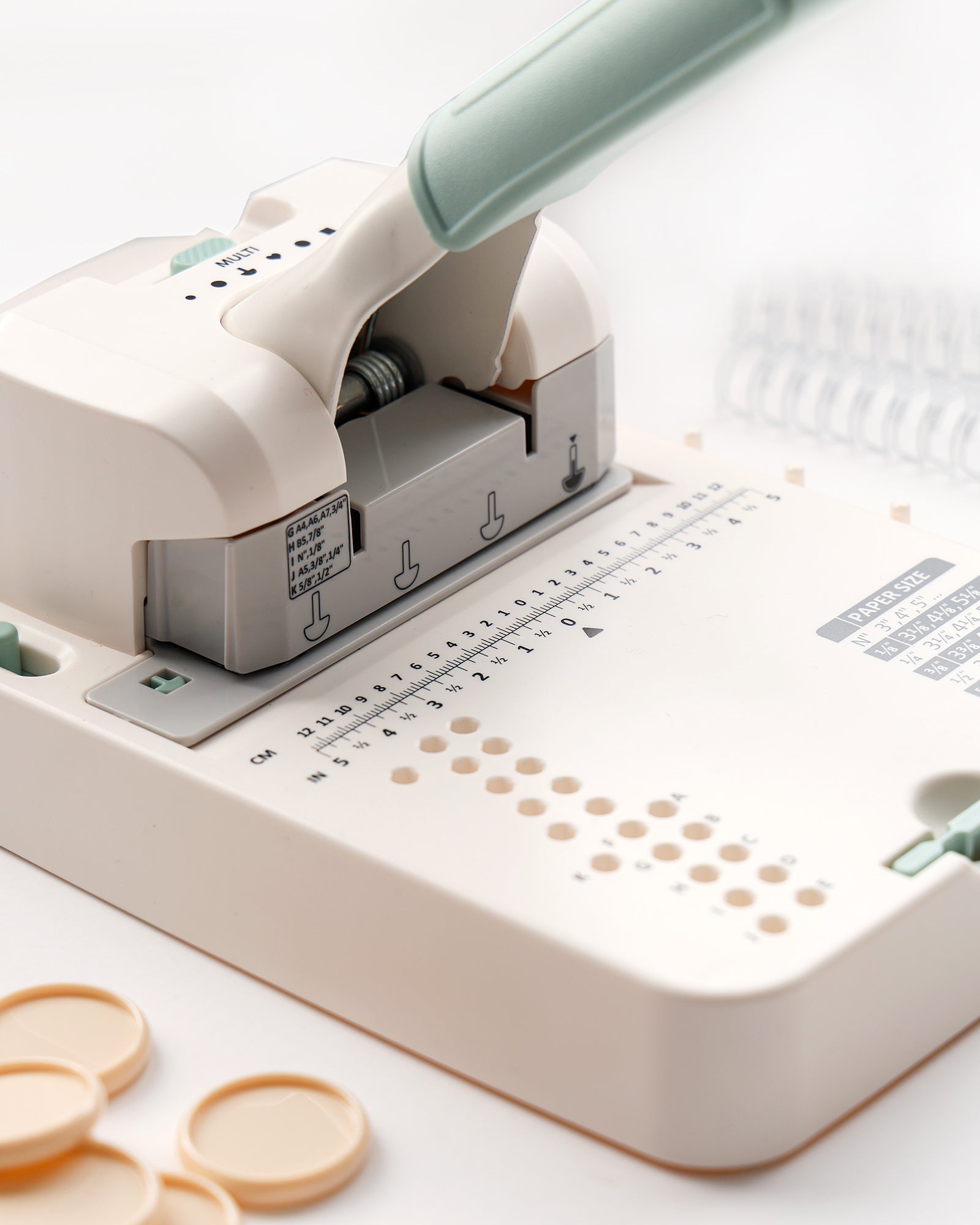 Nahaufnahme einer weißen Papierstanzmaschine mit einem Griff, Führungsmarkierungen und runden gestanzten Papierstücken in der Nähe.