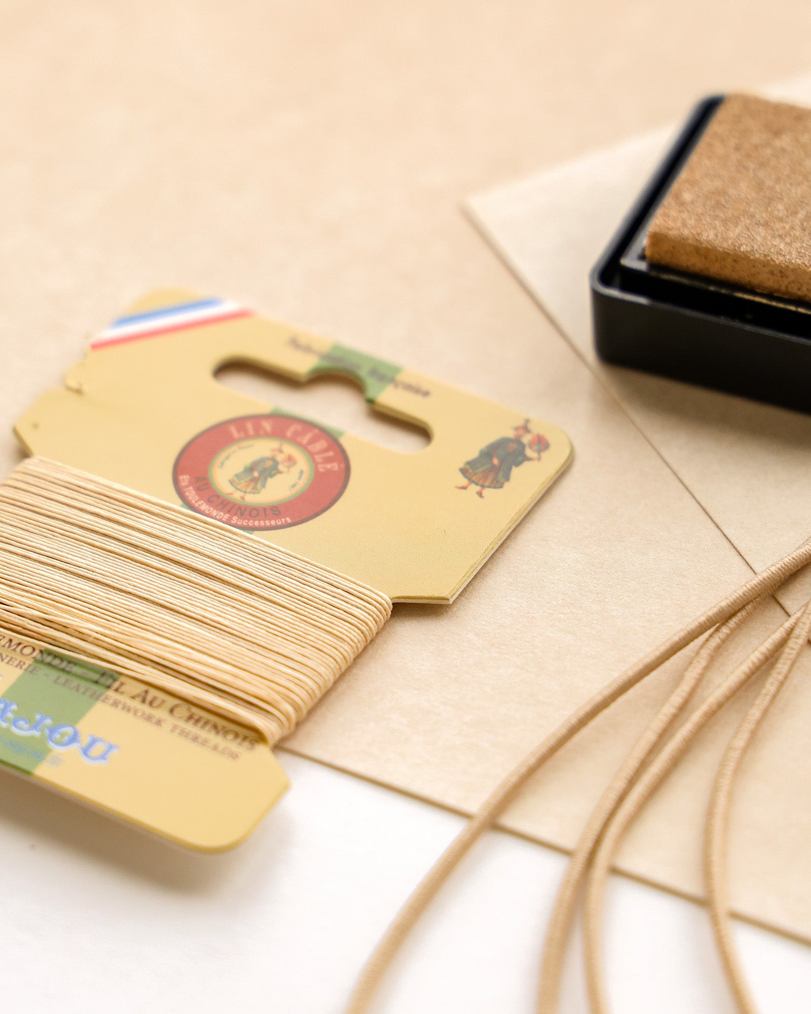 Beigefarbenes Garn, Kartonverpackung, Stempelkissen und hellbraune Kordel auf einer hellen Oberfläche.