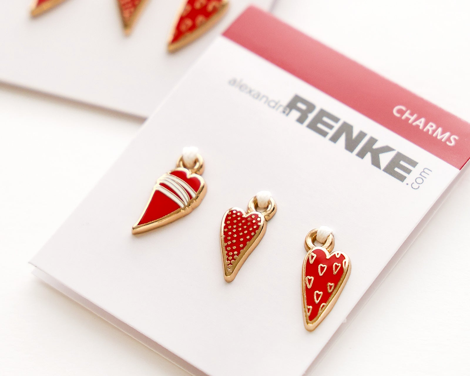 Zwei Sets mit roten und goldenen Anhängern in Herzform auf weißen Karten der Marke Alexandra Renke.