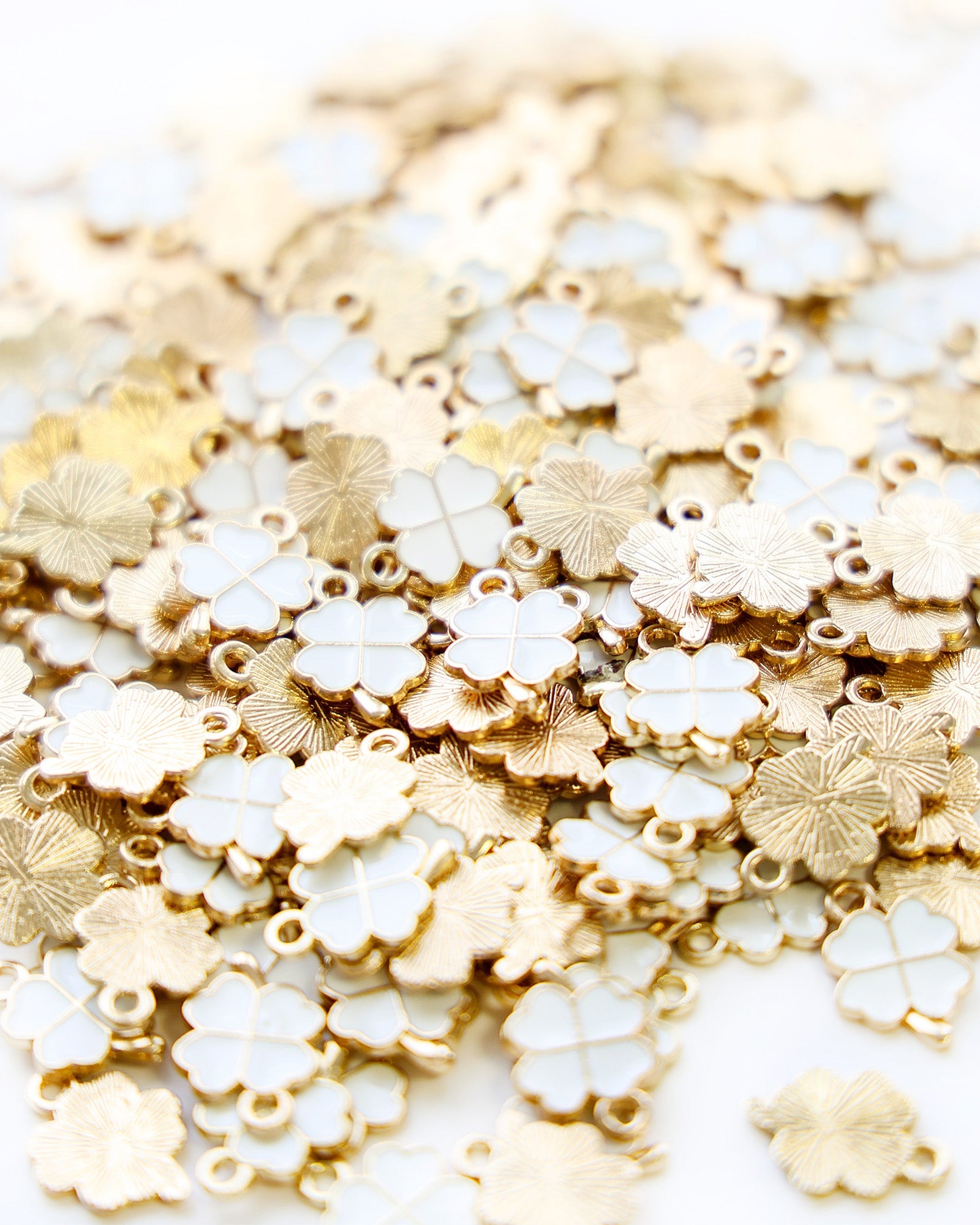 Ein Stapel goldfarbener und weißer vierblättriger Kleeblätter, die dicht an dicht verstreut sind.