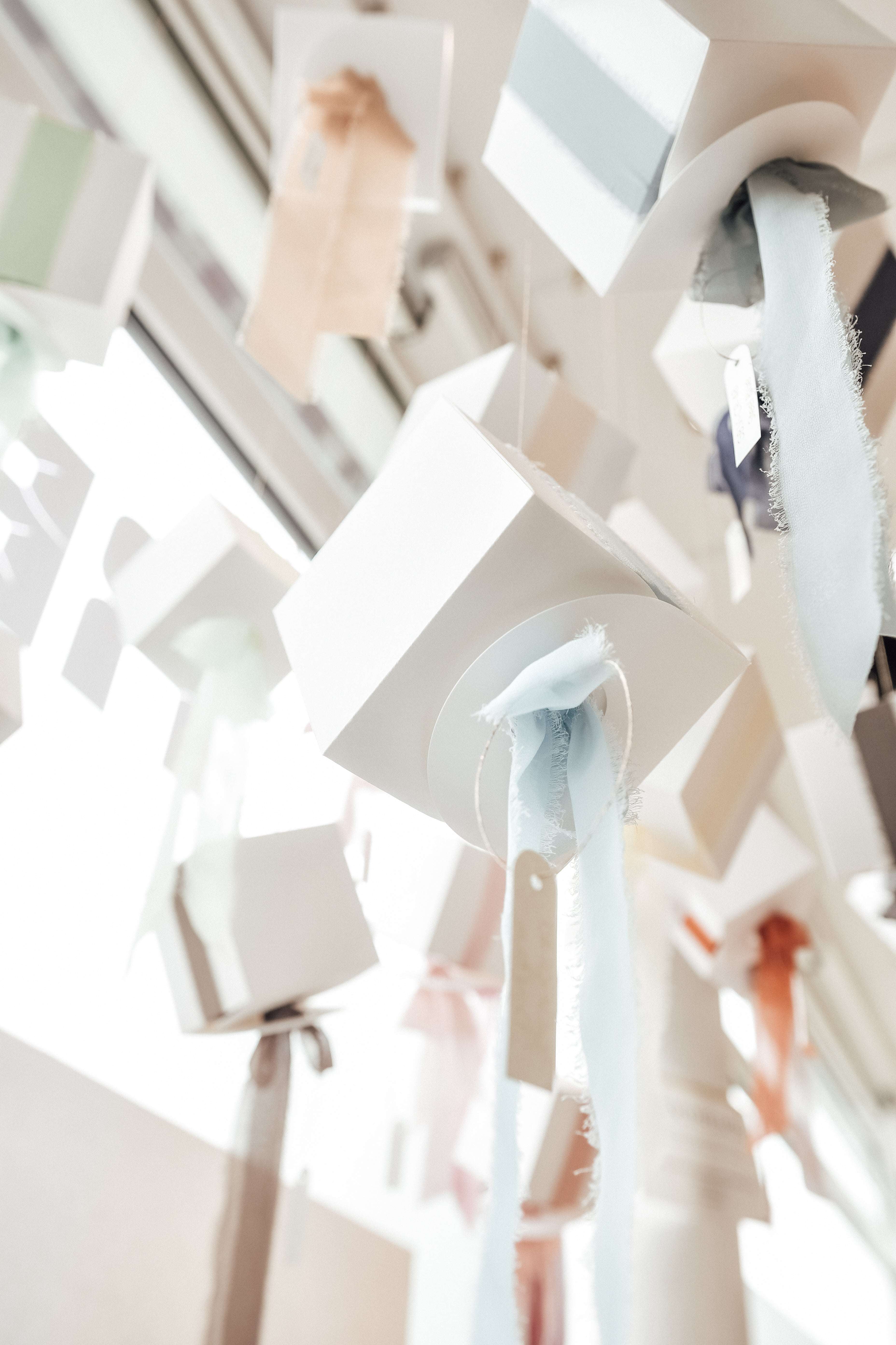 Weiße Schulabschlusskappen mit pastellfarbenen Quasten hängen von der Decke, von einem niedrigen Winkel aus gesehen in hellem Licht.