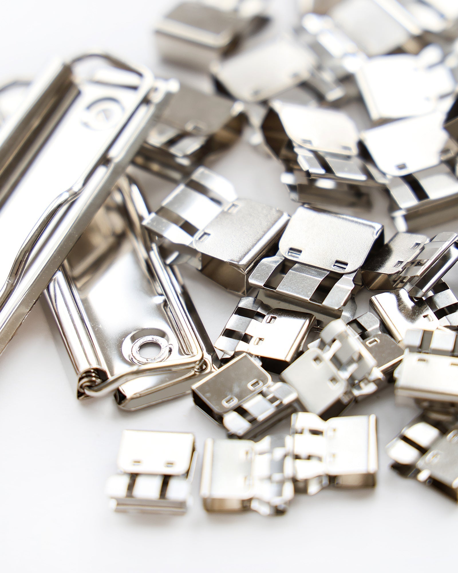 Ein Stapel silbern glänzender Heftklammern und Verschlüsse aus Metall auf einer weißen Fläche.