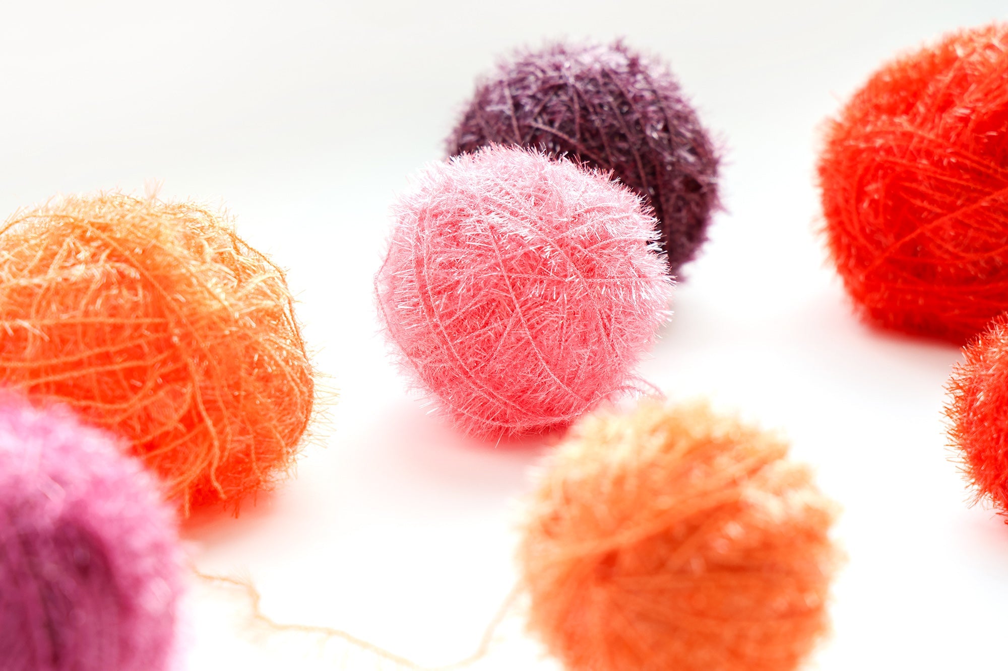Bunte Garnkugeln, darunter rosa, orange, rot und lila, angeordnet auf einer weißen Fläche.