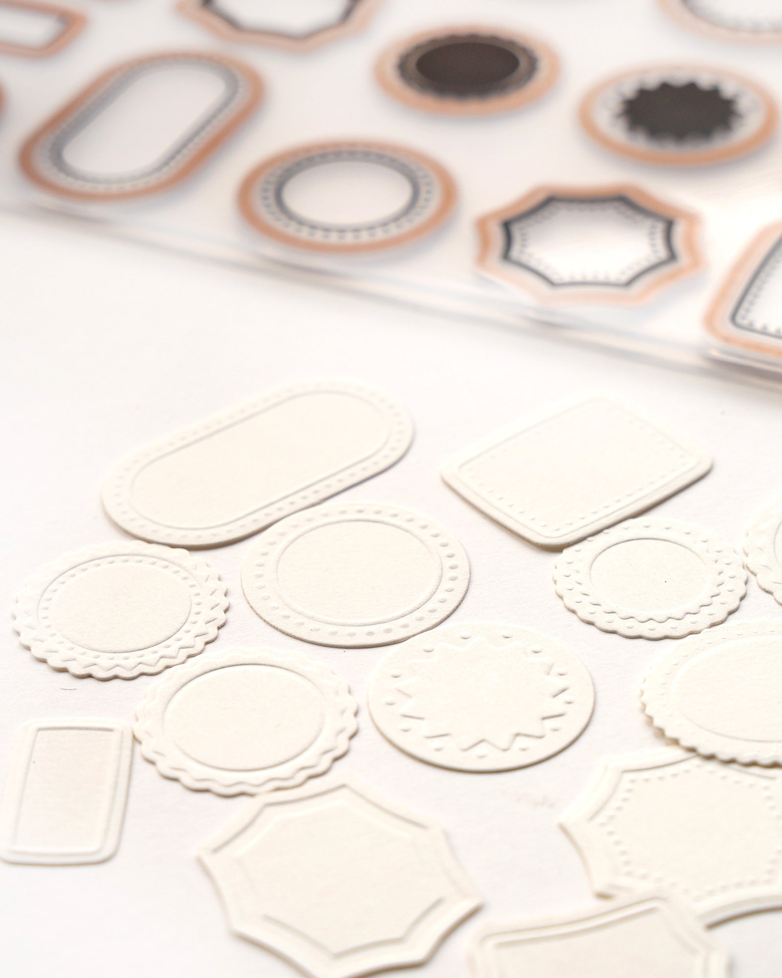 Verschiedene leere, geprägte weiße Papieretiketten und Formen auf einer weißen Fläche mit einem Bogen Briefmarken darüber.