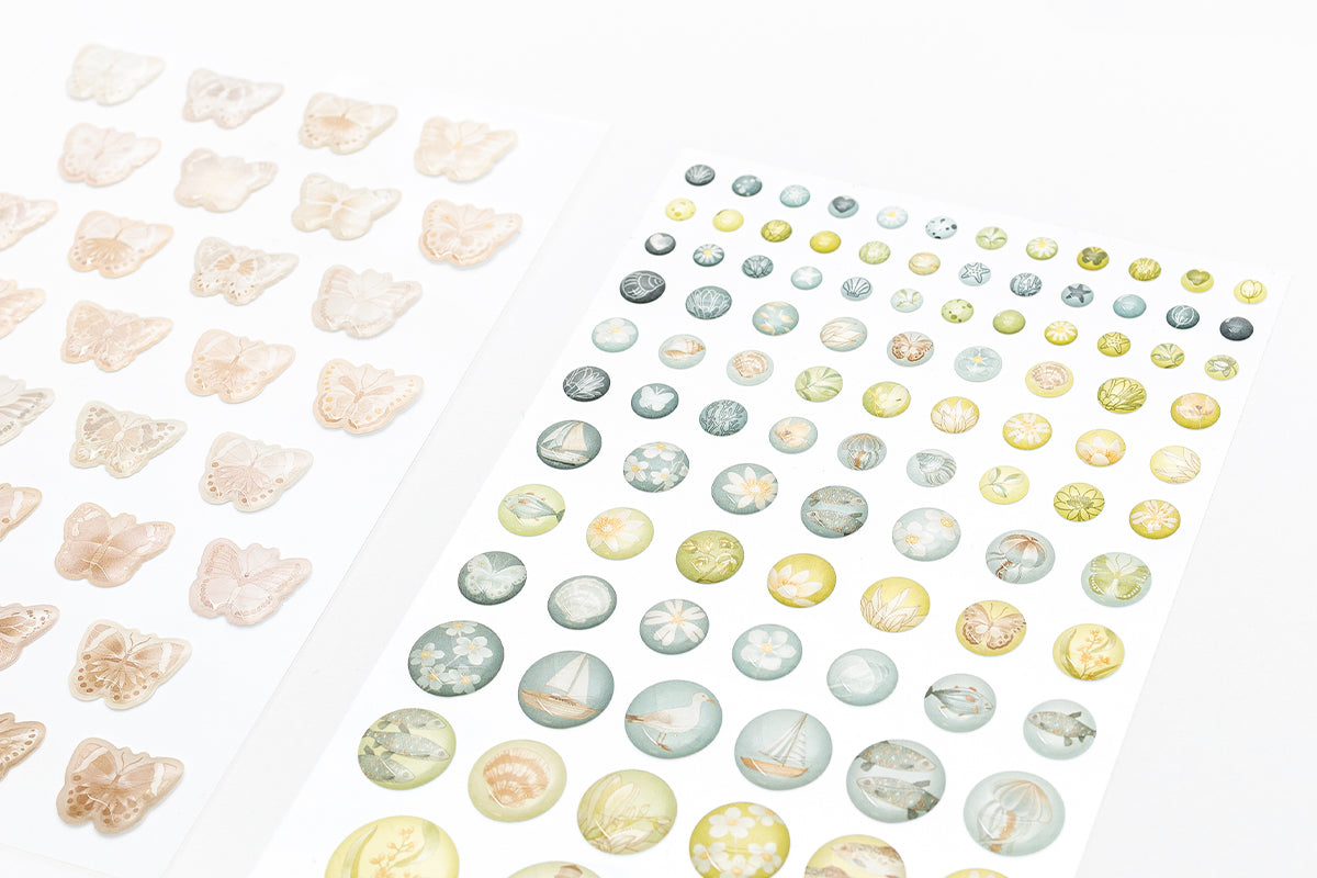 Blätter aus dekorativem Papier mit pastellfarbenen Motiven zum Thema Meer, darunter Fische, Muscheln und Segelboote.