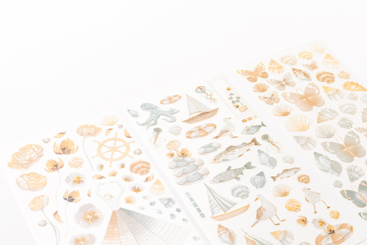 Blätter aus dekorativem Papier mit pastellfarbenen Motiven zum Thema Meer, darunter Fische, Muscheln und Segelboote.