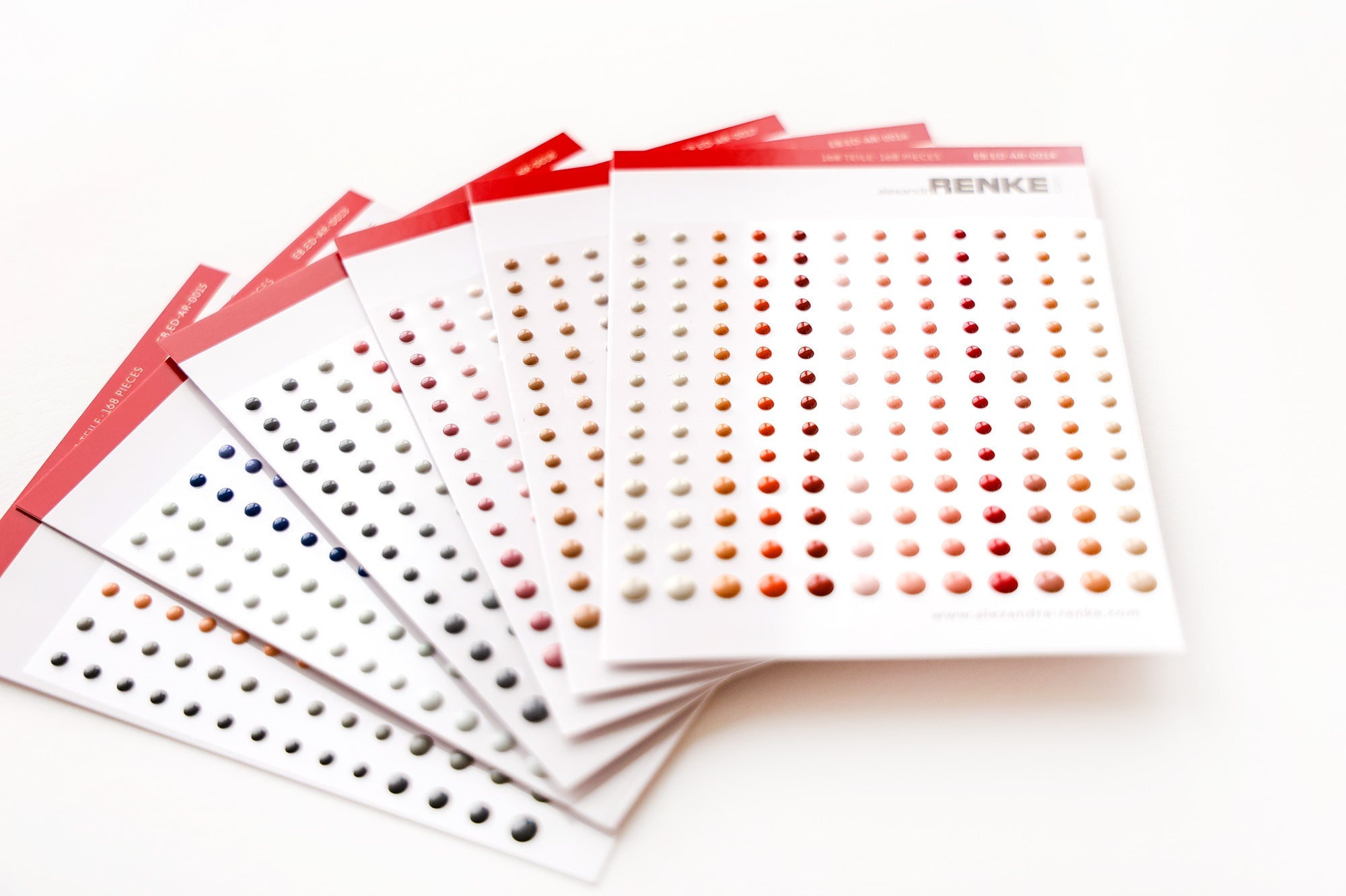 Bögen mit runden Klebepunkten in verschiedenen Farben, die in Reihen auf weißem Papier mit roten Kopfzeilen angeordnet sind.