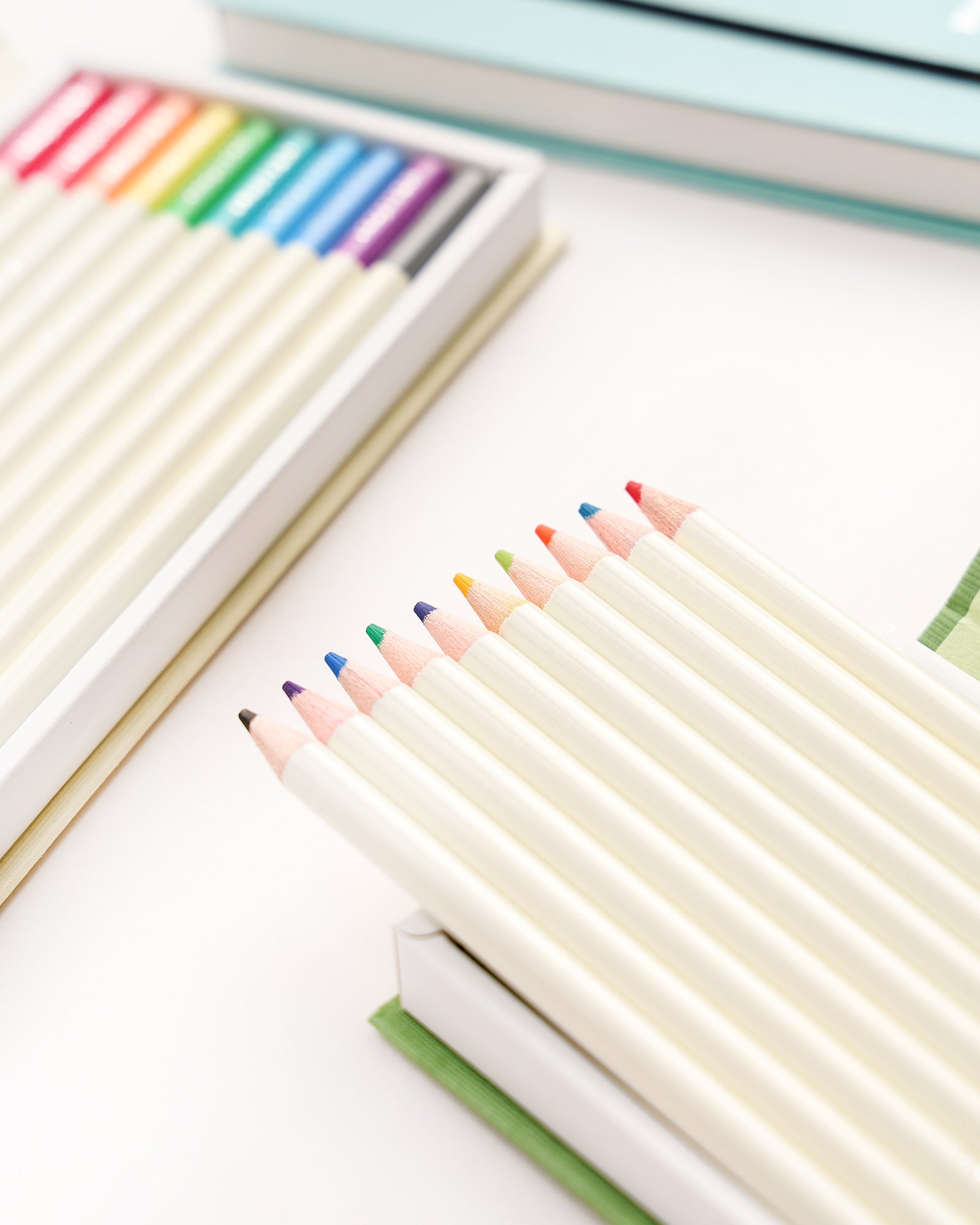 Schachtel mit weißen Buntstiften mit regenbogenfarbenen Spitzen, die ordentlich auf einer weißen Fläche angeordnet sind.