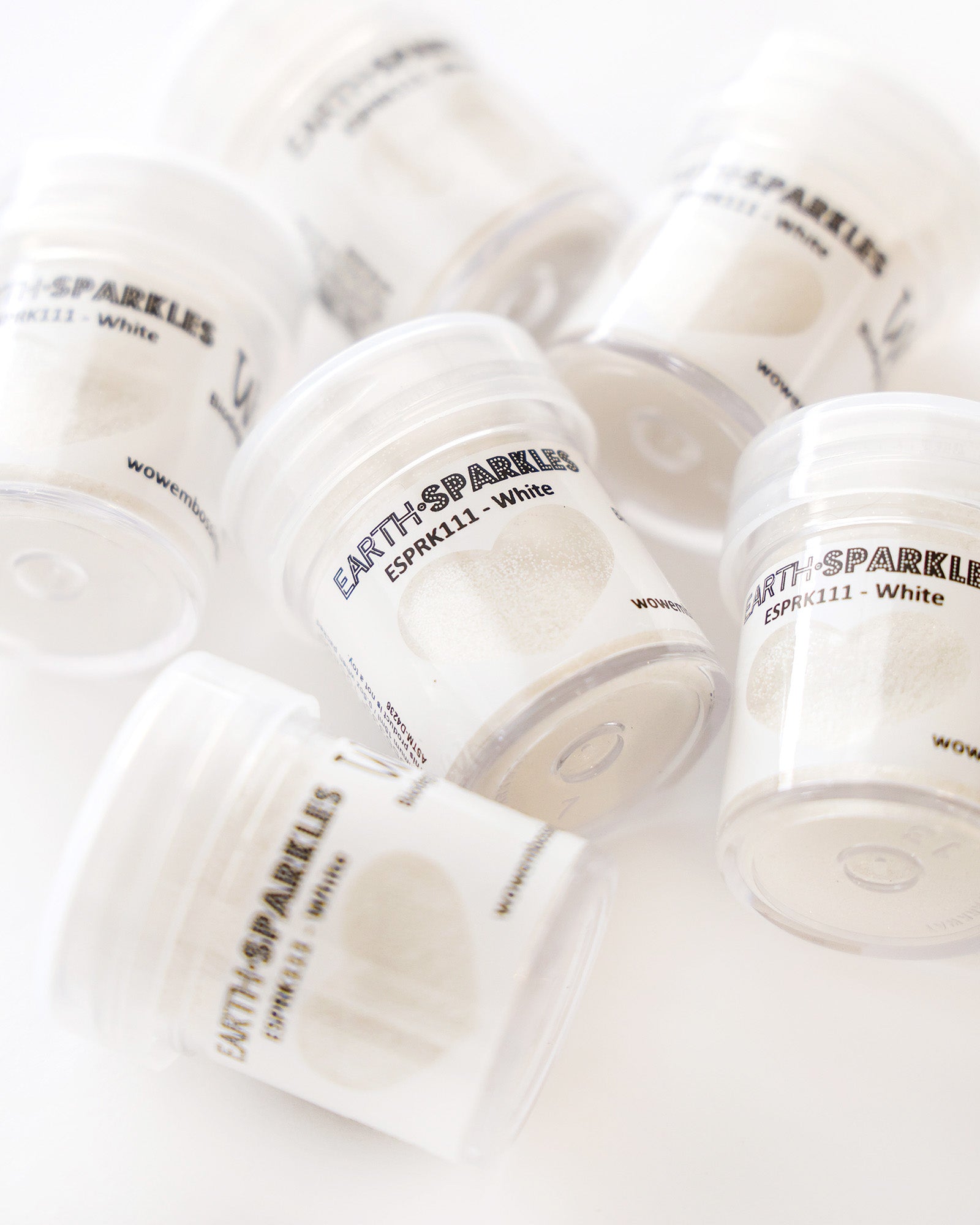 Kleine durchsichtige Gläser mit der Aufschrift EARTH SPARKLES White auf einer weißen Fläche verstreut.