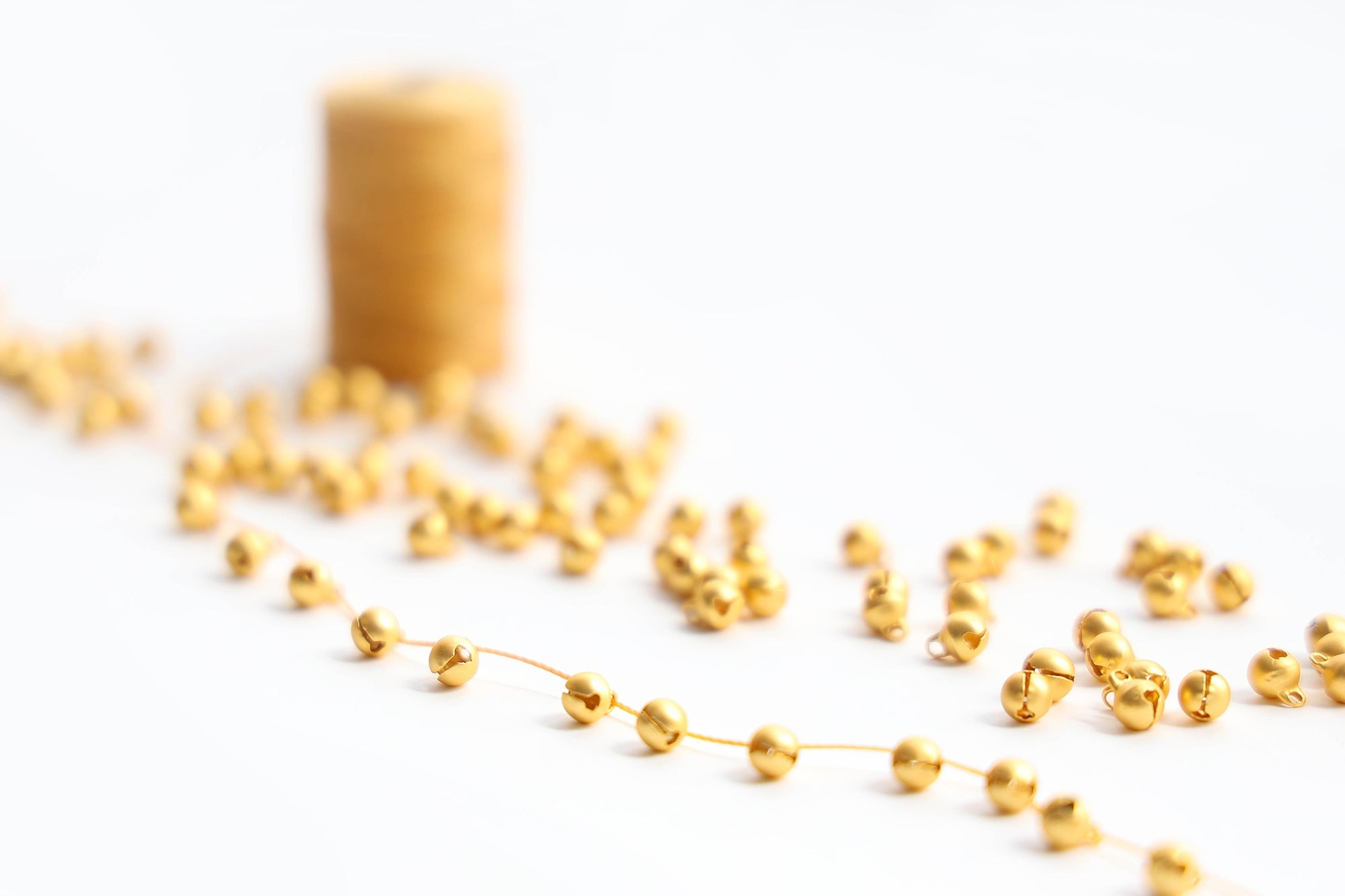 Nahaufnahme von glänzenden Goldperlen auf einer Schnur, mit einer Spule mit Goldfaden im Hintergrund.