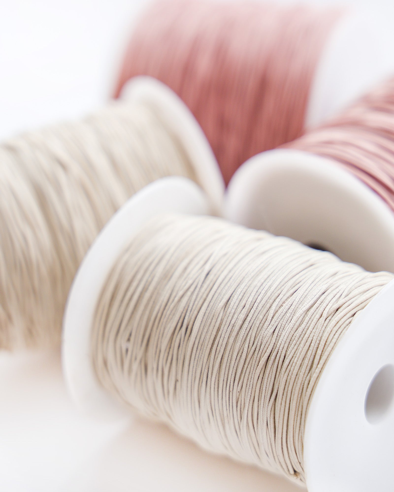 Nahaufnahme von drei Garnspulen in den Farben Creme, Rosa und Beige auf weißem Hintergrund.