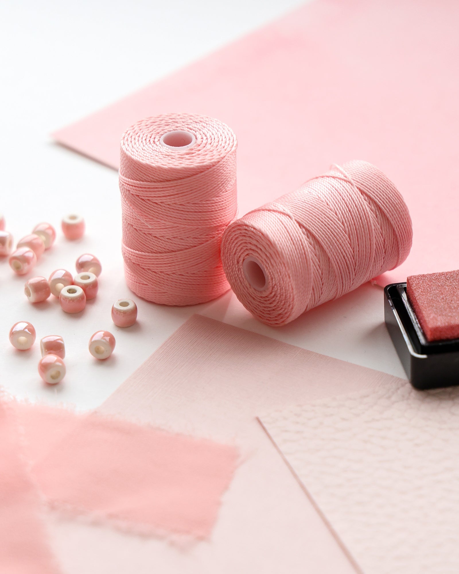 Rosa Fadenspulen, rosa Perlen und rosa Bastelmaterialien, die auf einer hellen Fläche angeordnet sind.