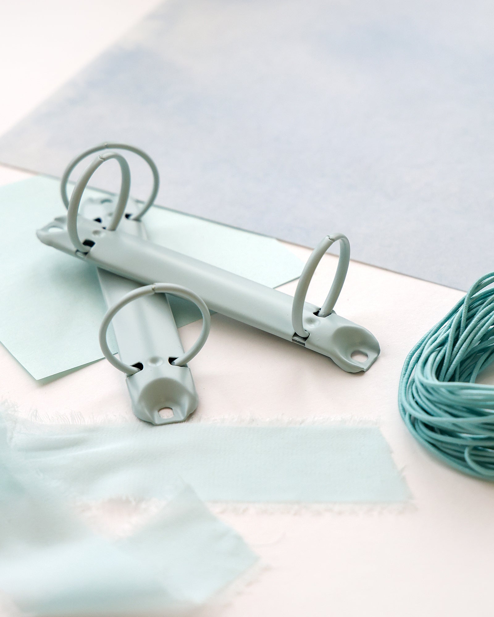 Zwei offene hellblaue Binderinge, umgeben von pastellblauem Papier, Stoff und Schnur.