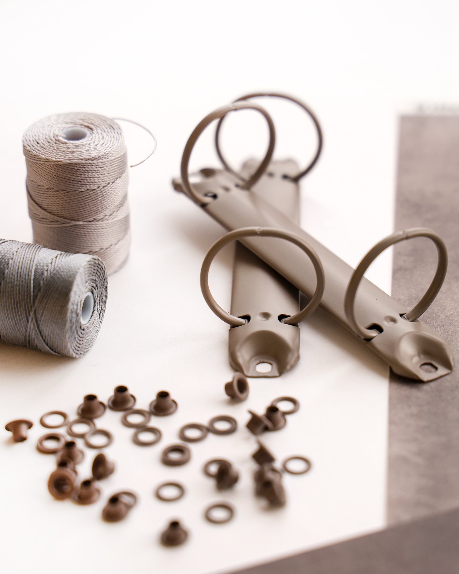 Zwei Binderinge aus Metall, Fadenspulen und verschiedene kleine Metallteile, die auf einer weißen Fläche angeordnet sind.