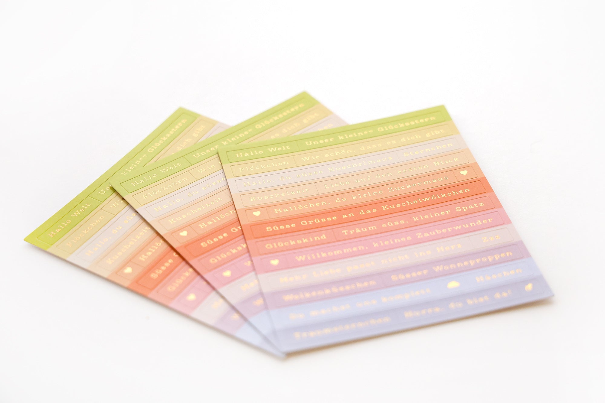 Vier pastellfarbene Blätter mit deutschen Sätzen, aufgefächert auf weißem Hintergrund.