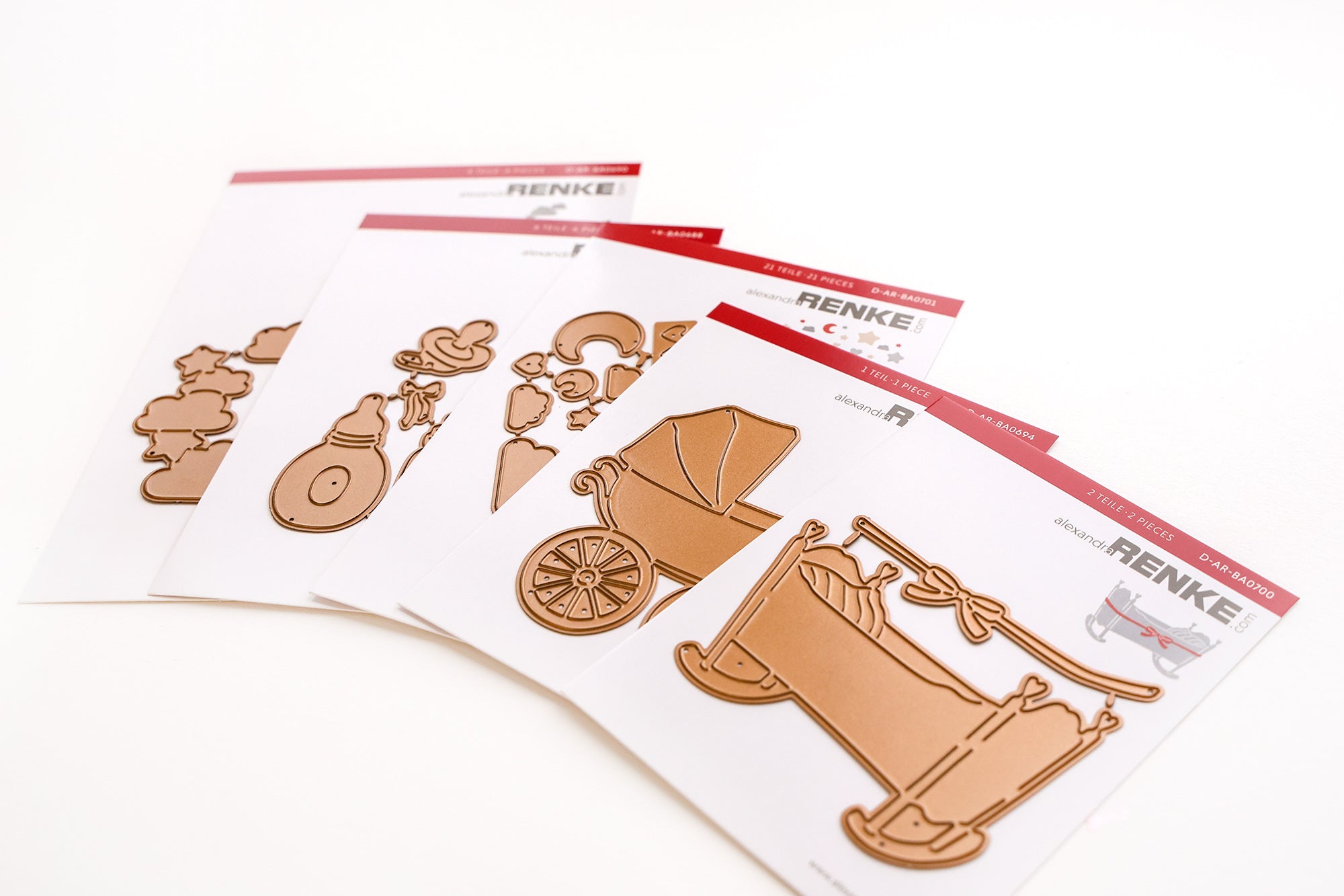 Vier Sets mit Metallstempeln auf weißen Karten mit Motiven rund ums Baby wie Kinderwagen und Krippe.