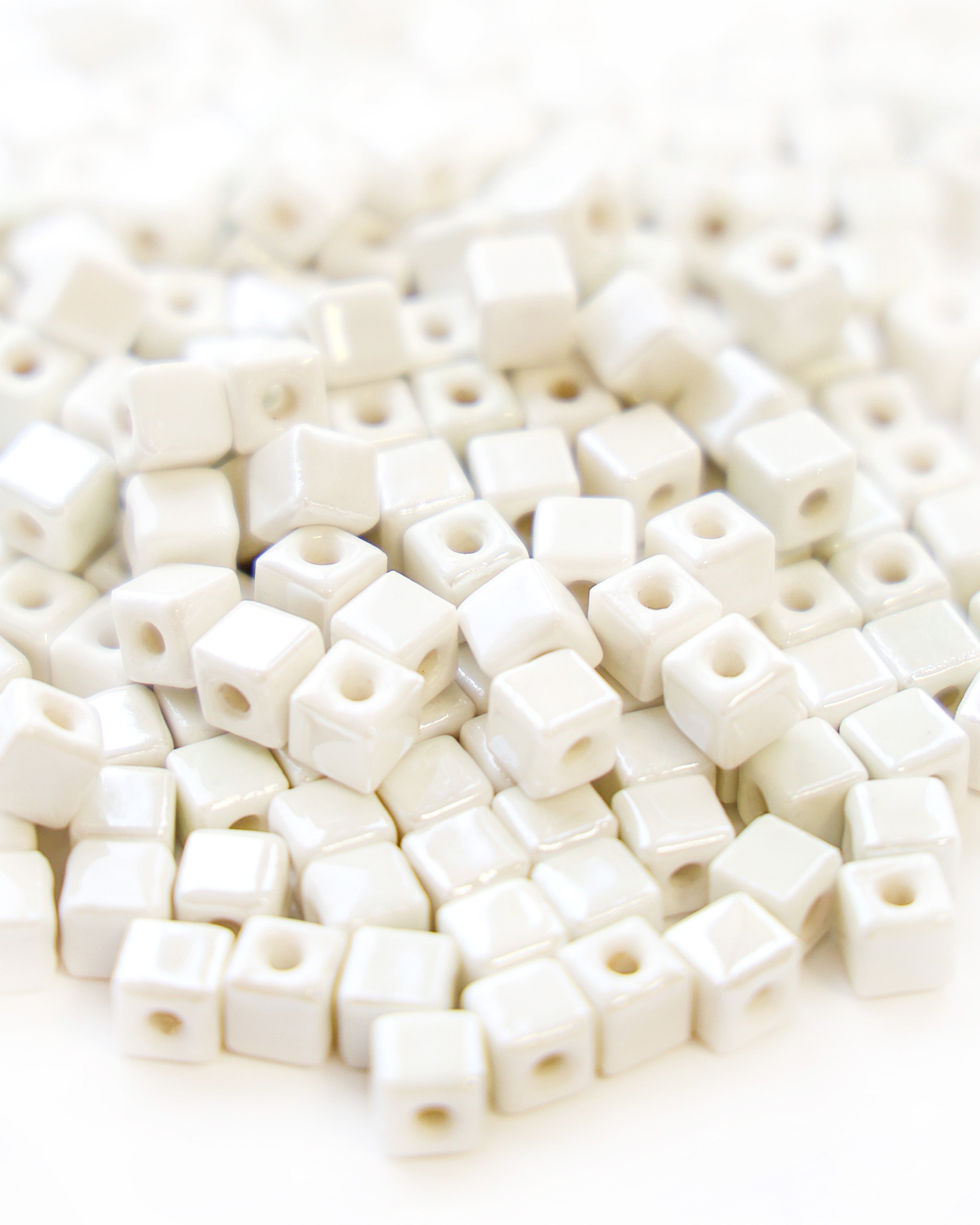 Ein Stapel glänzender weißer, quadratischer Perlen mit Löchern in der Mitte, die dicht an dicht gestapelt sind.