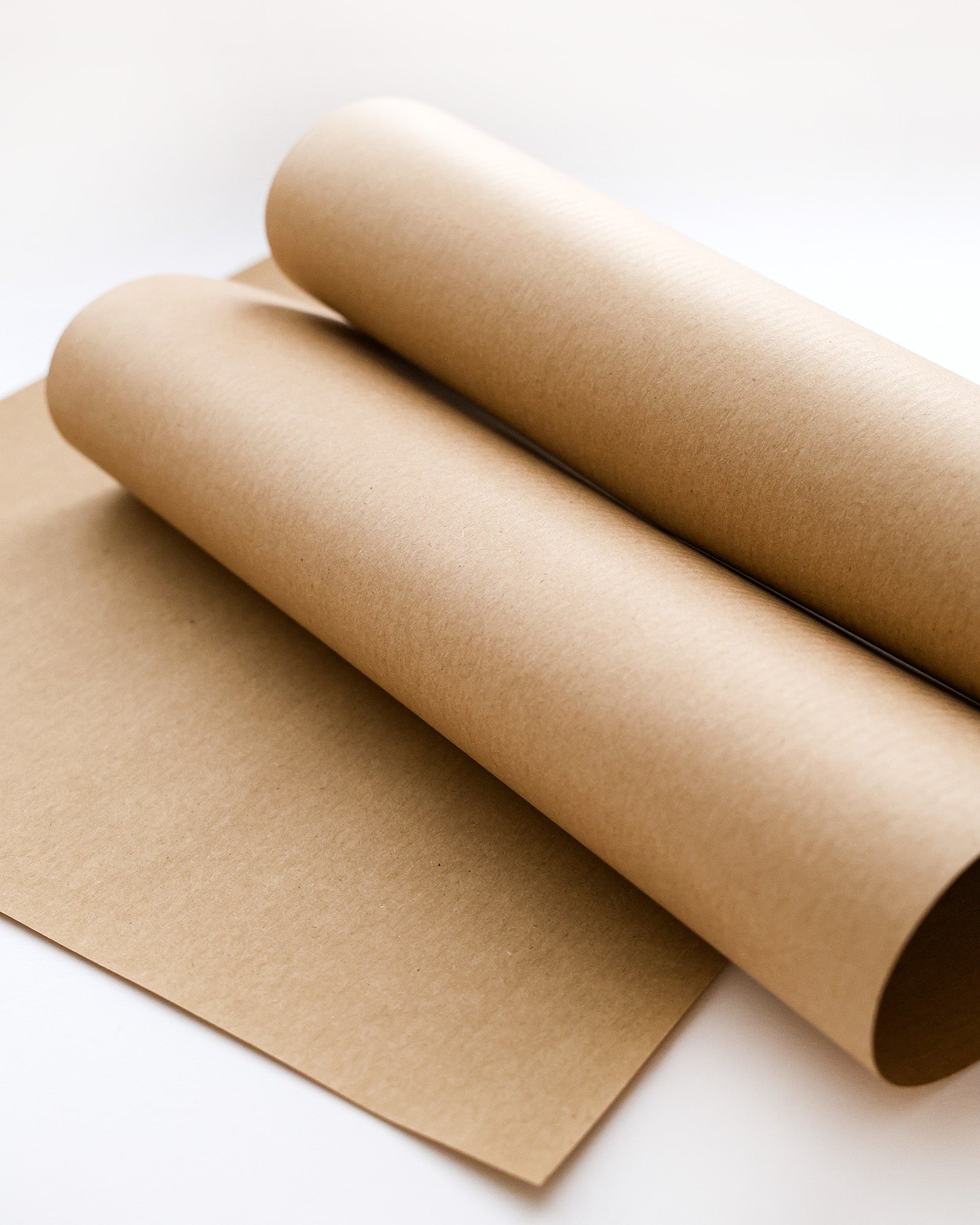 Zwei Rollen braunes Kraftpapier auf einem flachen braunen Kraftpapierbogen vor weißem Hintergrund.