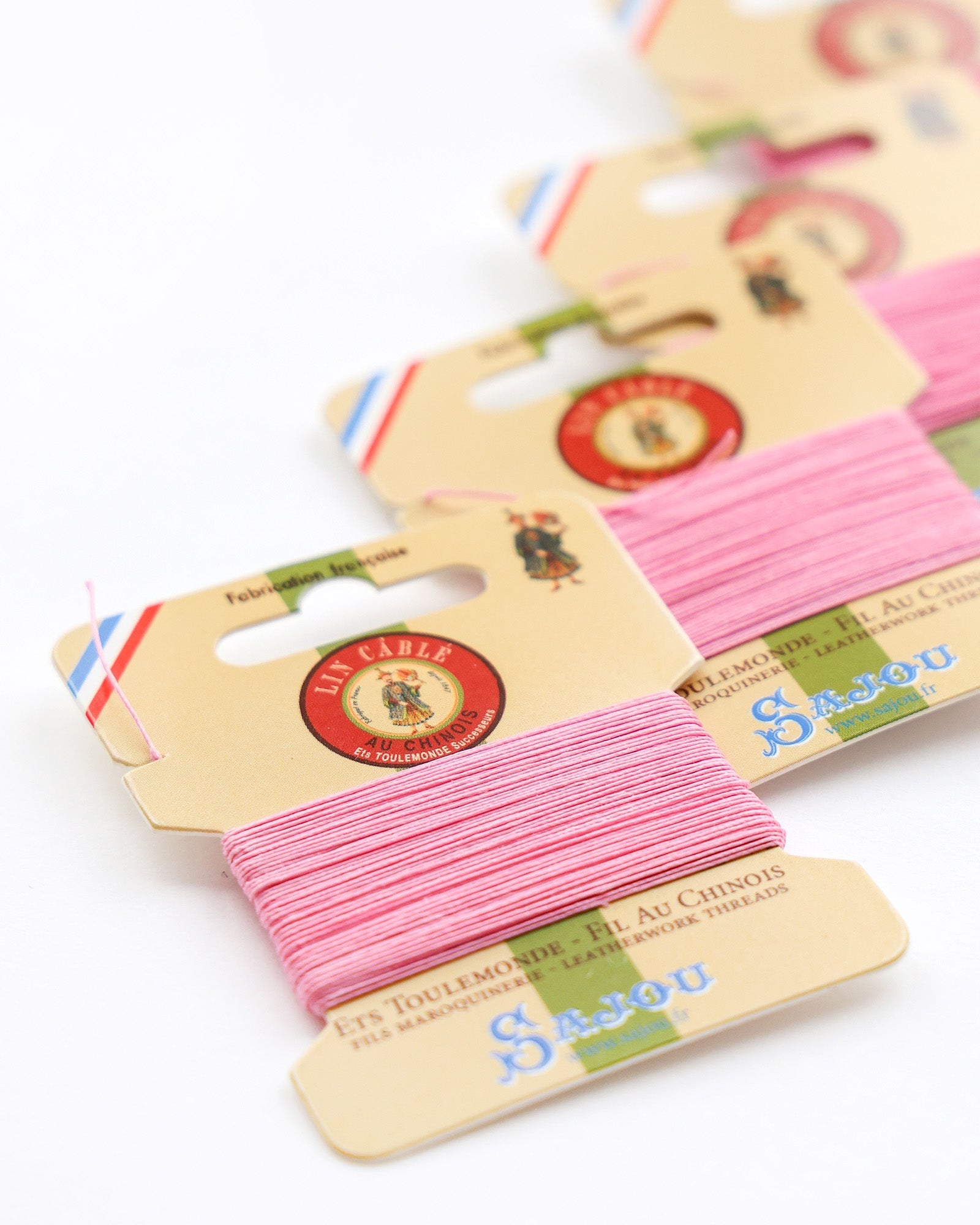 Vier Karten mit rosafarbenem Stickgarn sind ordentlich in einer diagonalen Reihe auf einer weißen Fläche angeordnet.
