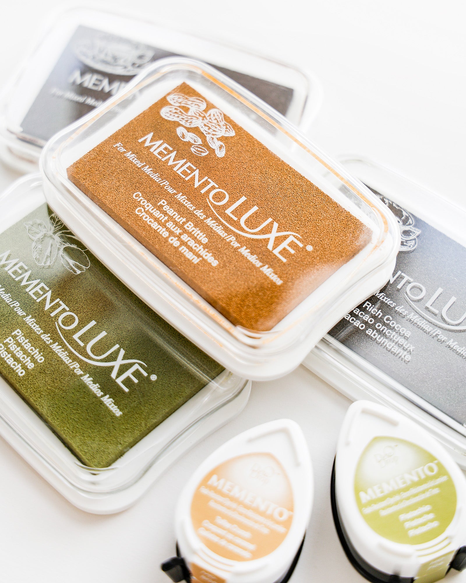 Drei MementoLUXE-Farbkissen in Braun, Grün und Schwarz sowie zwei kleine Memento-Farbkissen in Weiß und Gelb.