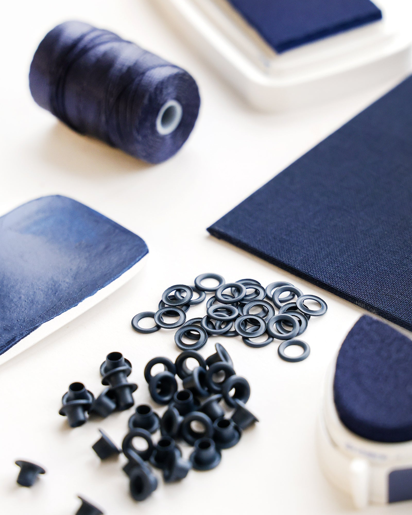 Marineblaues Nähzubehör, darunter Garn, Stoff, Ösen und ein Stempelkissen, angeordnet auf einer weißen Fläche.